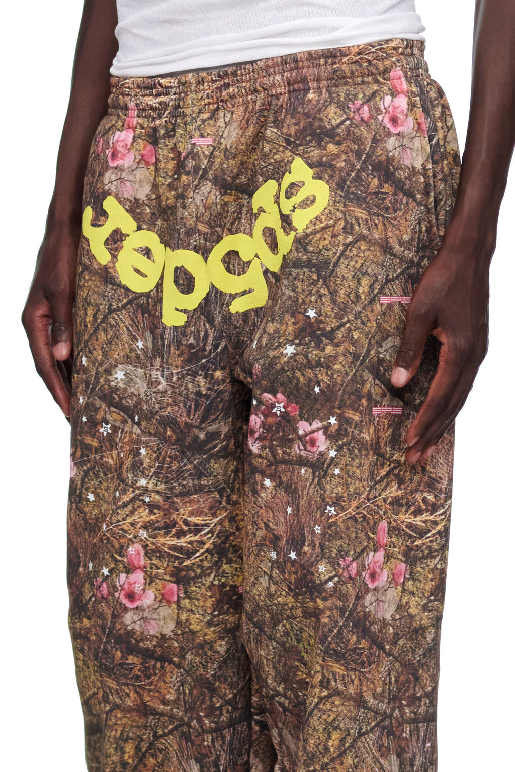 REAL TREE OG WEB SWEATPANT: Brown camo fleece sweatpants with pink flowers, white stars, and yellow puff print "sp5der" text.