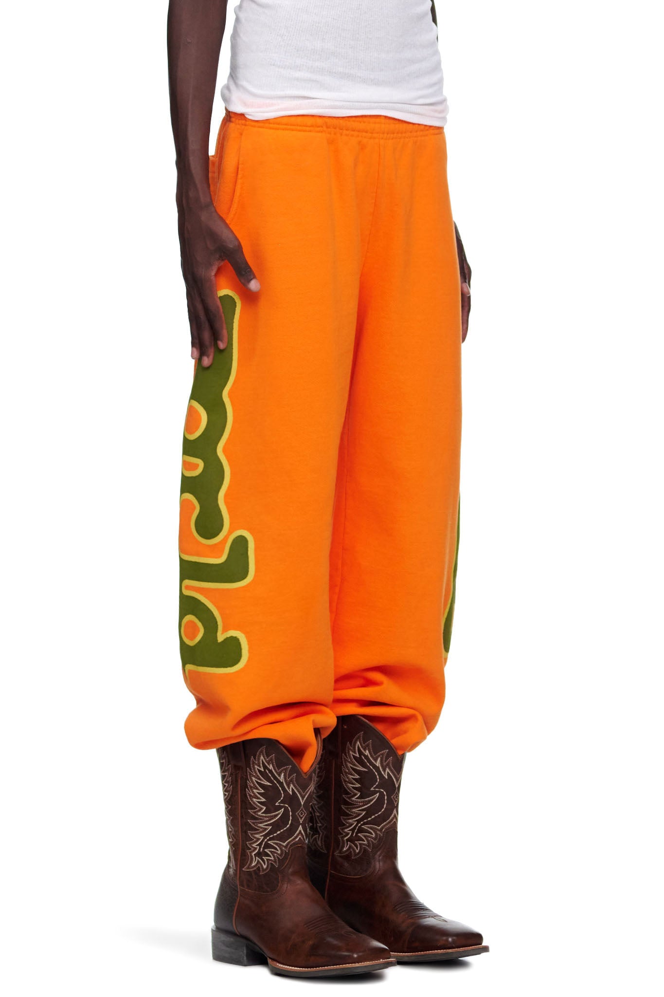 Orange BELUGA SWEATPANT with green 'Worldwide' puff print, worn by a male model with cowboy boots.
