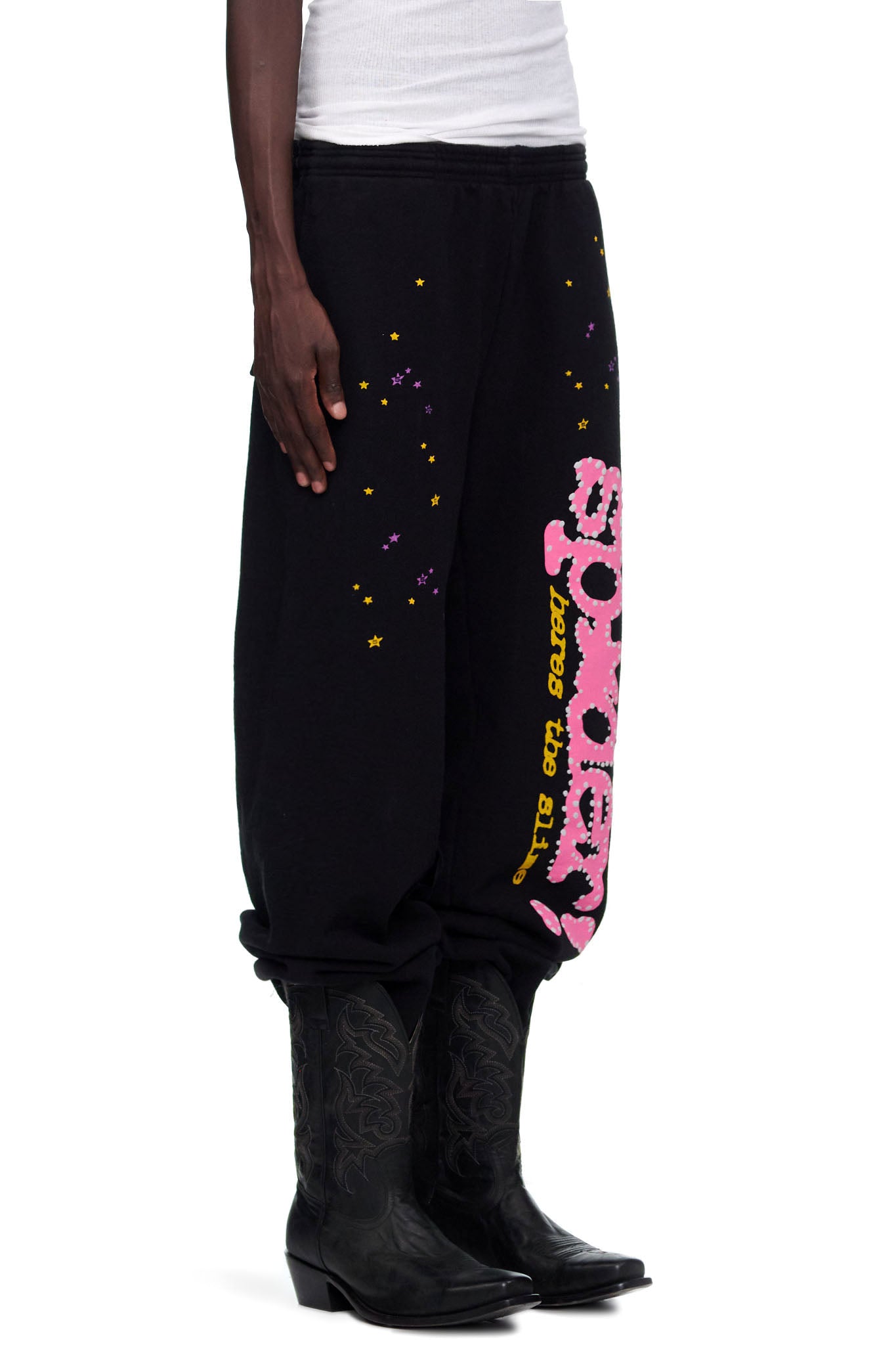 Black SP5DER V2 sweatpants with pink puff print, yellow and purple stars, worn by a male model.