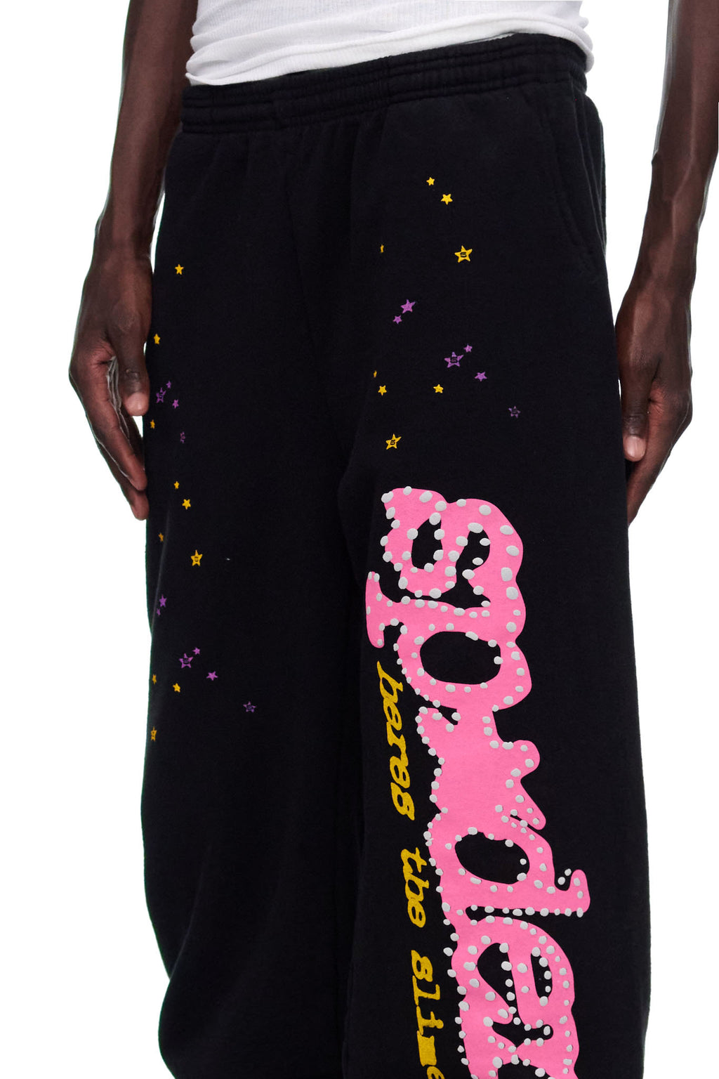 Black fleece sweatpants with pink puff print "SP5DER" motif, yellow and purple star prints.