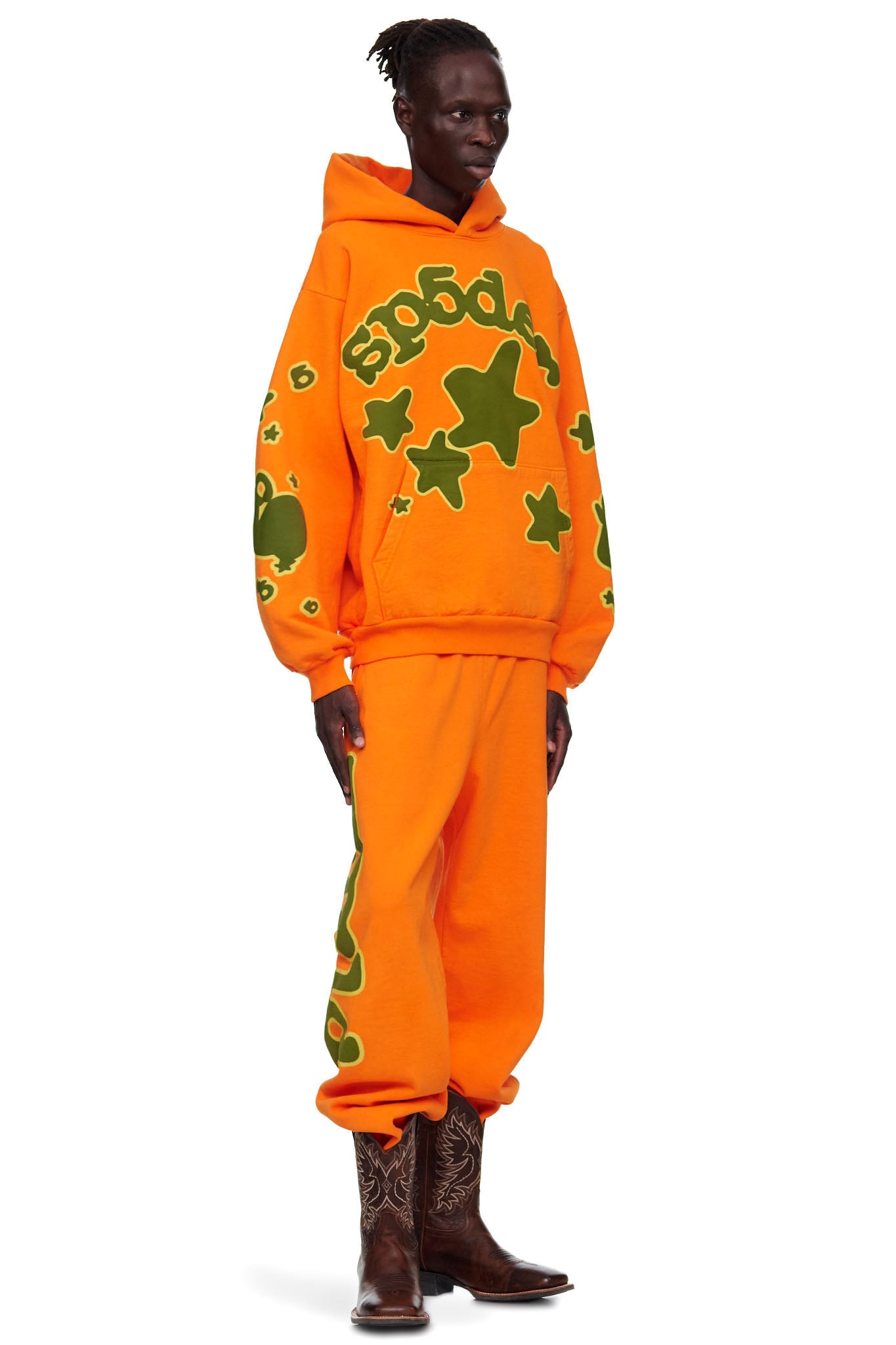Male model in orange BELUGA HOODIE and sweatpants with green 'SP5DER' and star puff print.