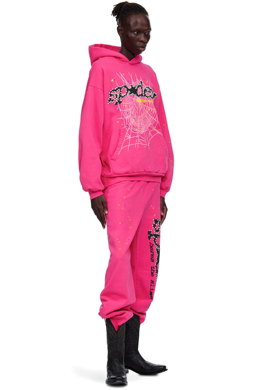 Male model in a pink fleece hoodie and sweatpants with SP5DER motif, spiderweb, and star prints.