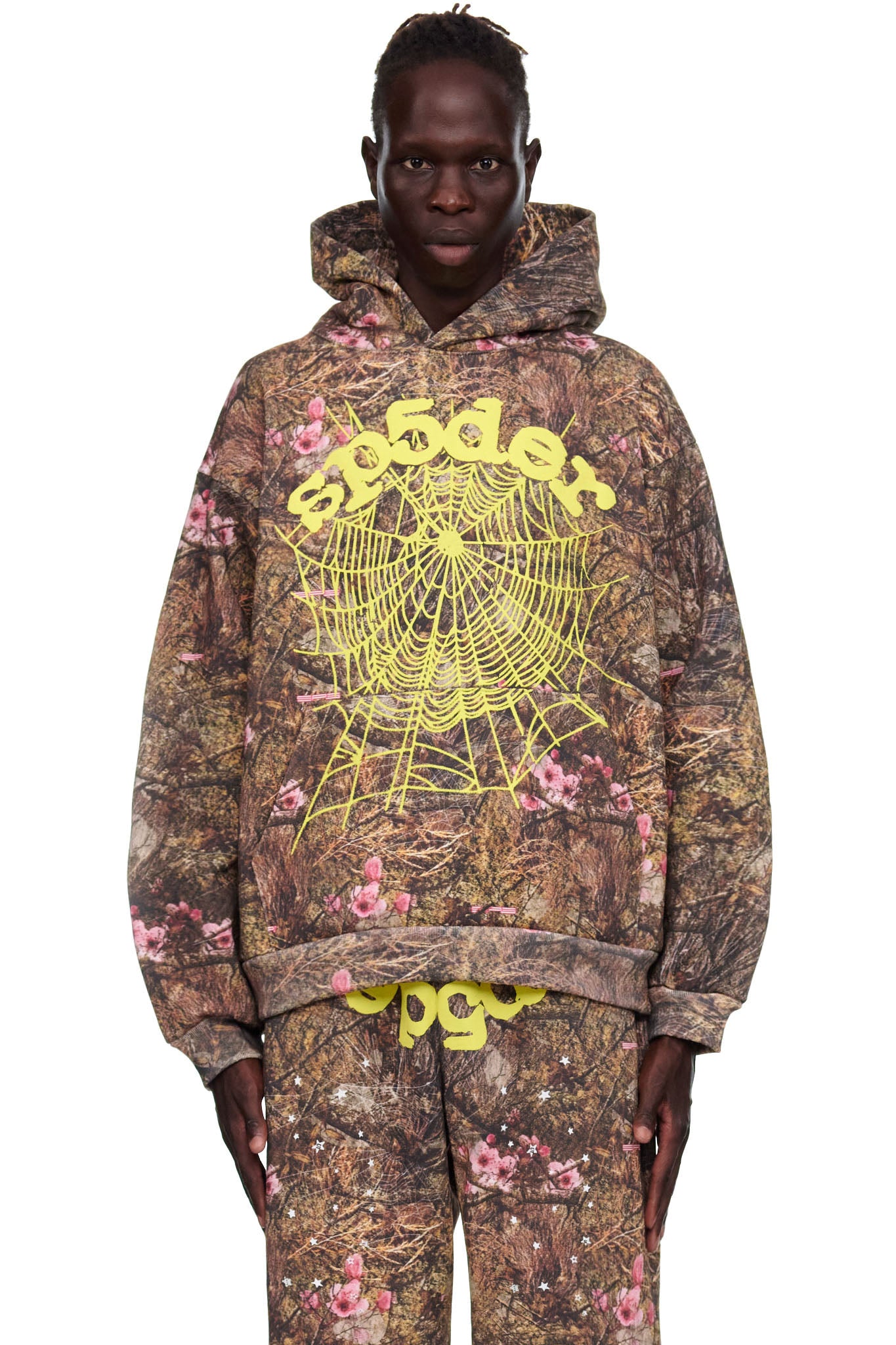 Male model in Real Tree OG Web Hoodie, a brown camo fleece with pink flowers, yellow "Sp5der" text, and a large spider web print.