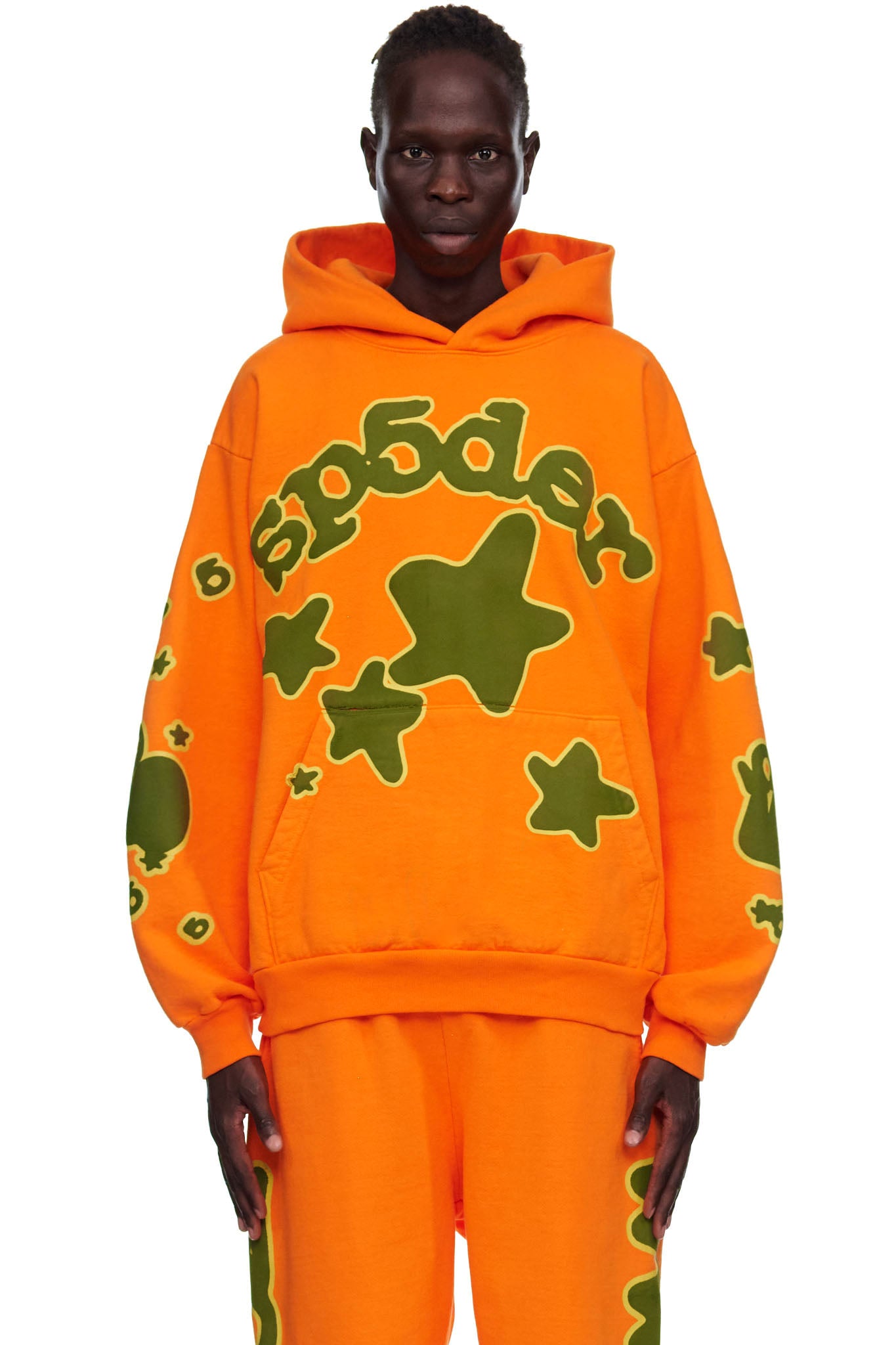 Male model in orange 23oz fleece BELUGA HOODIE with green 'SP5DER' and star puff print.