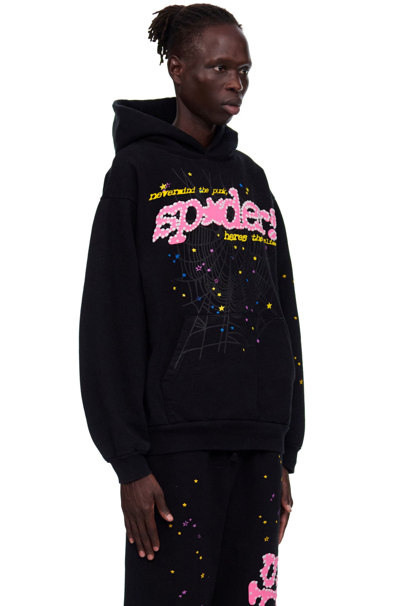 Male model in black 23oz fleece hoodie with pink puff print "sp5der" logo, spider web, and colorful star prints.