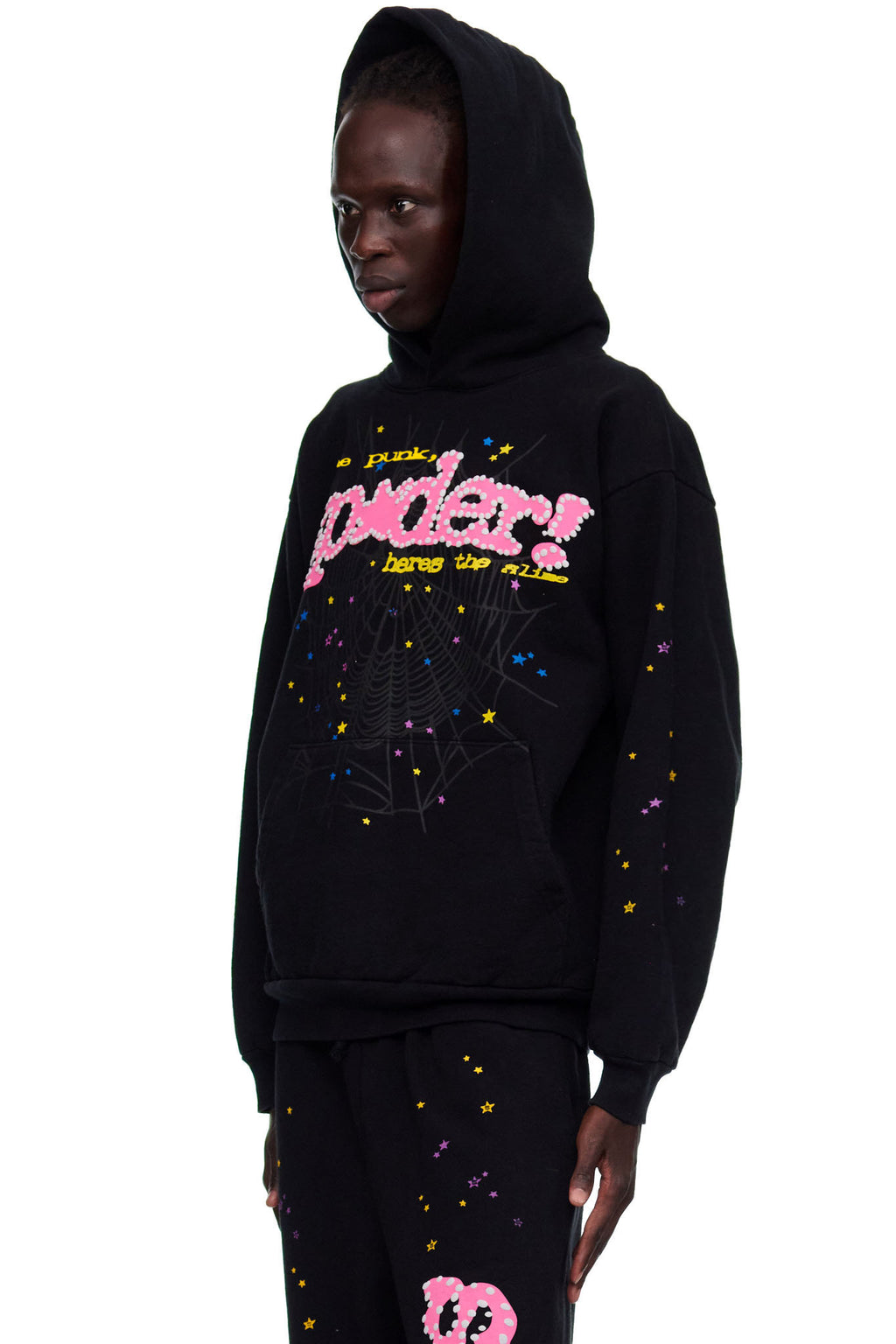 Black fleece hoodie with pink "SP5DER" puff print, web, and colorful star designs. Male model wears size L.