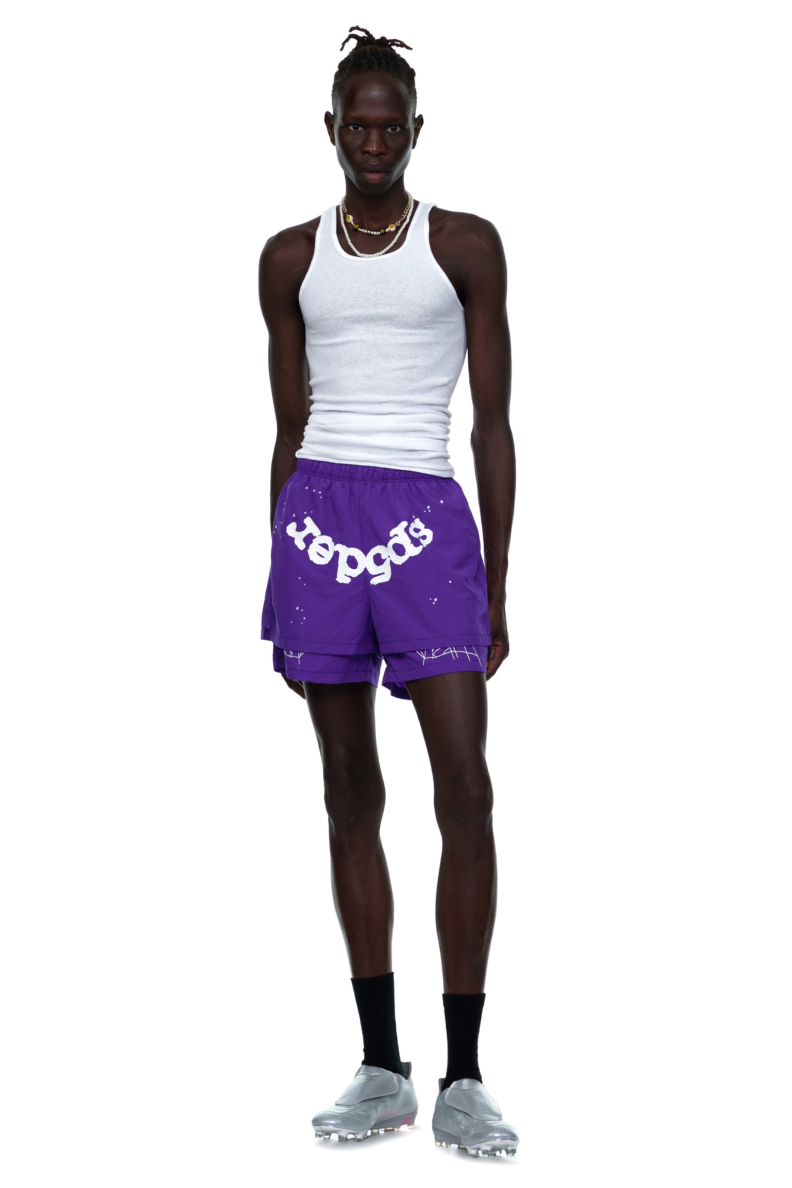 Model in purple nylon GRAPE LOGO SHORT with white "sp5der" text, high-low hem, and web print.