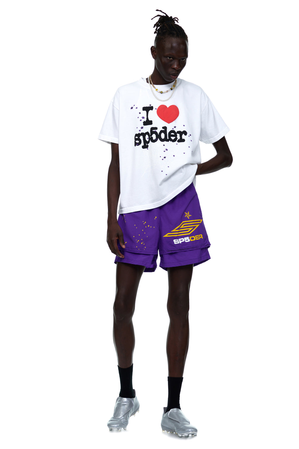 Men's white cotton tee with "I ❤️ SP5DER" graphic, paired with purple shorts and silver shoes.