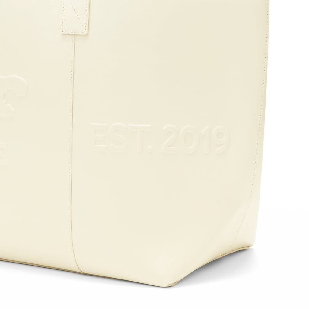 Cream genuine leather tote bag with "EST. 2019" embossed on the side panel.