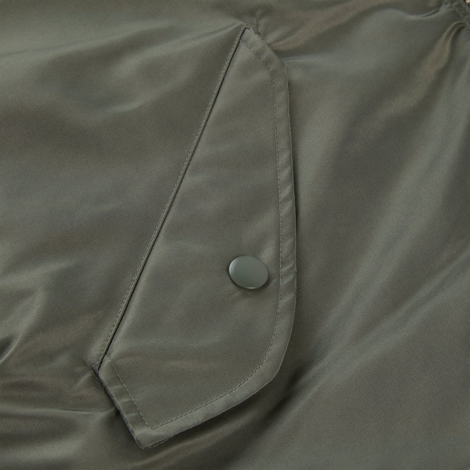 Close-up of an olive green nylon flight jacket with a snap-button flap pocket.