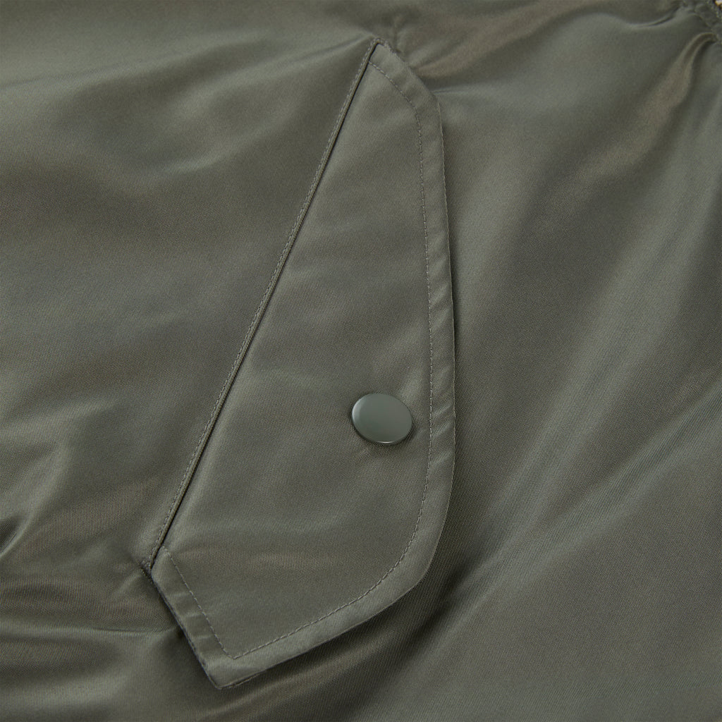Close-up of an olive green nylon flight jacket with a snap-button flap pocket.