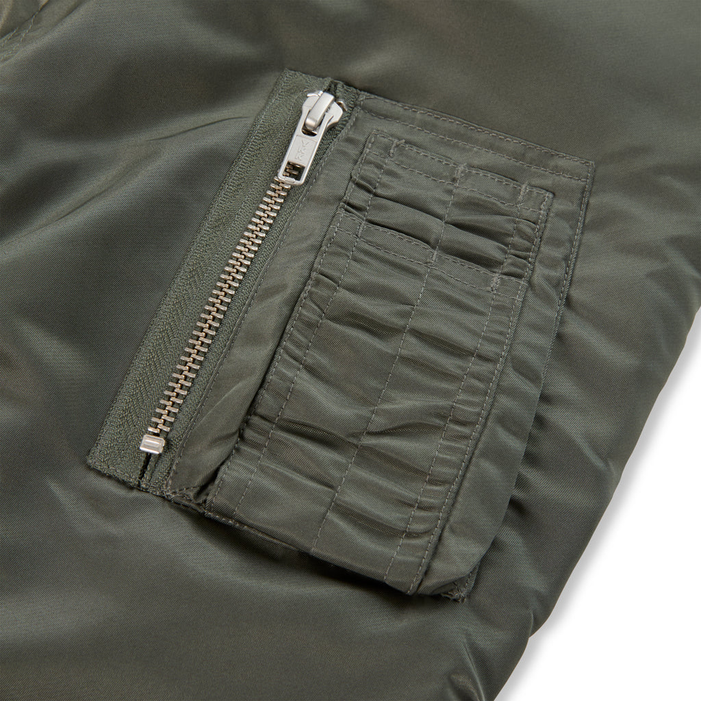 Olive green nylon bomber jacket sleeve with utility pocket and silver zipper.