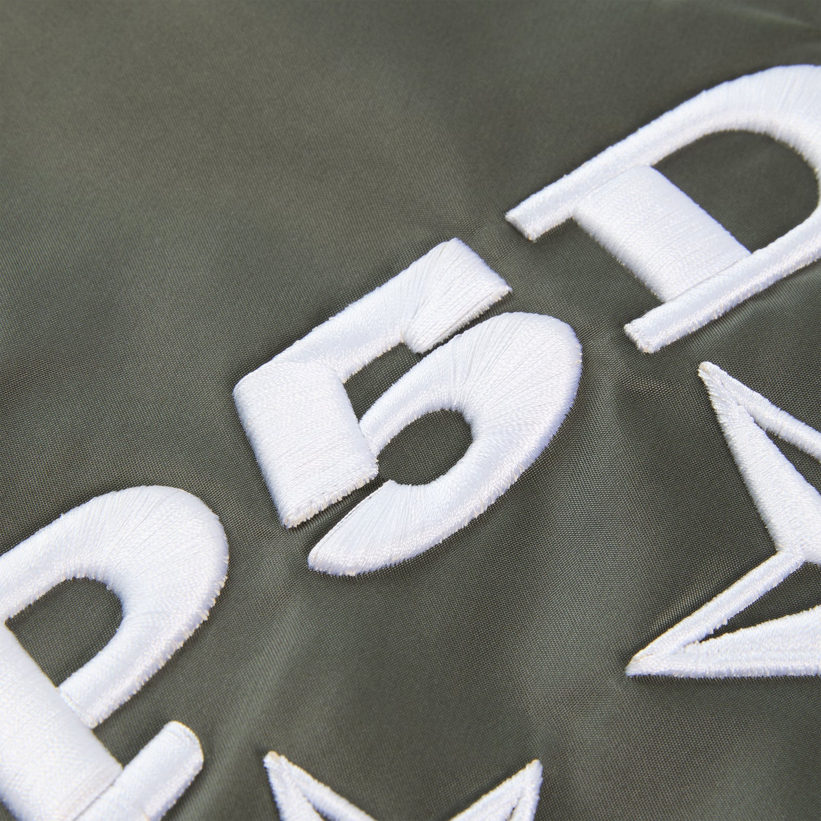 Close-up of olive green nylon flight jacket with bold white embroidered SP5DER graphic and star detailing.