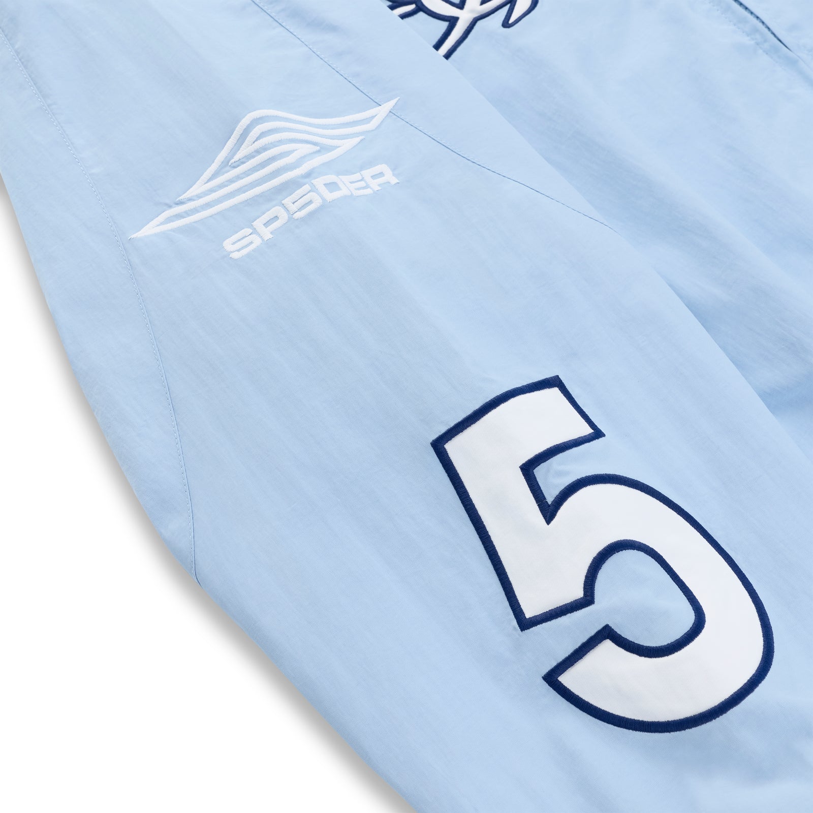 Light blue nylon track jacket sleeve with white "SP5DER" logo and large navy "5" graphic.