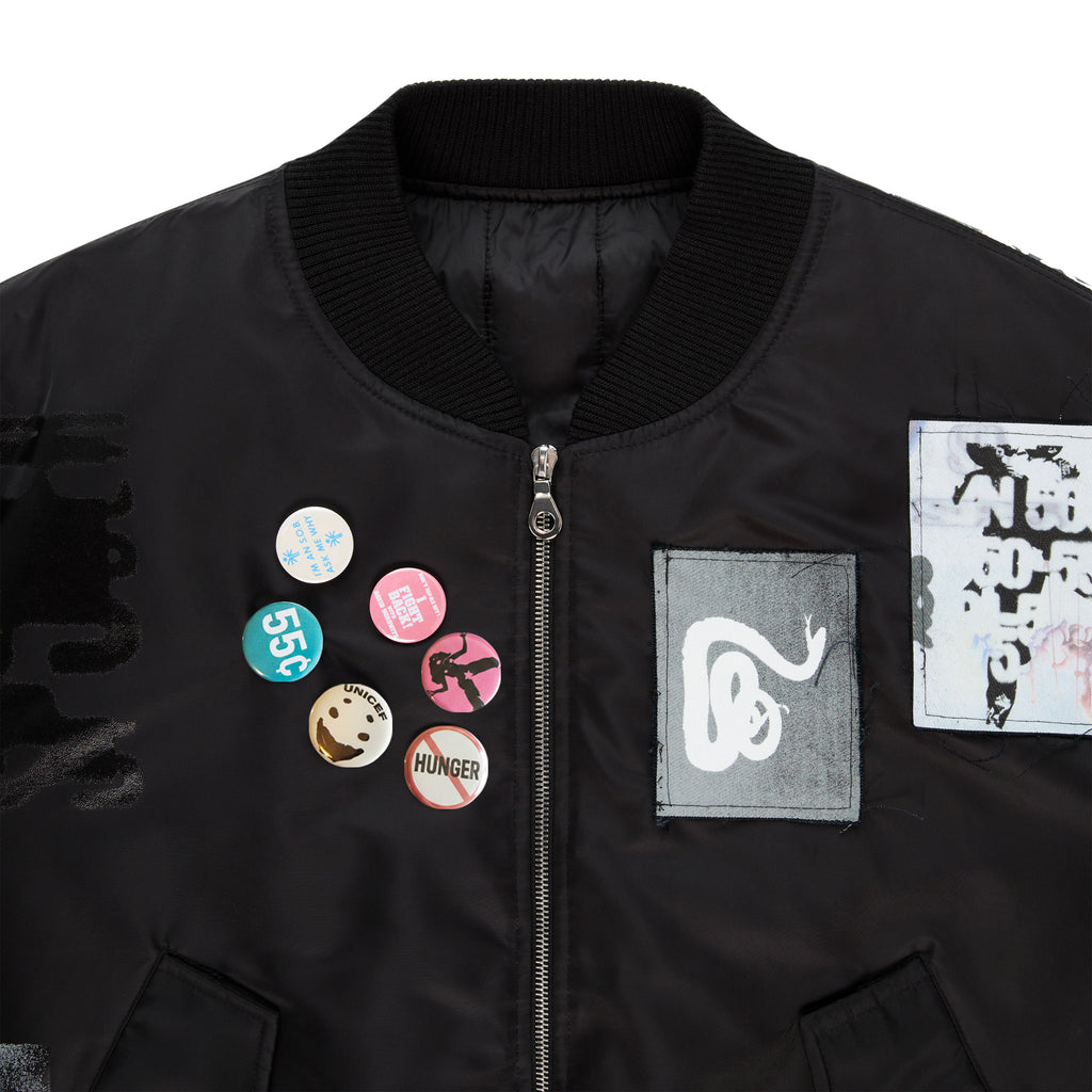 Black nylon satin bomber jacket with custom SP5DER patches, graphic print, and pins on chest.