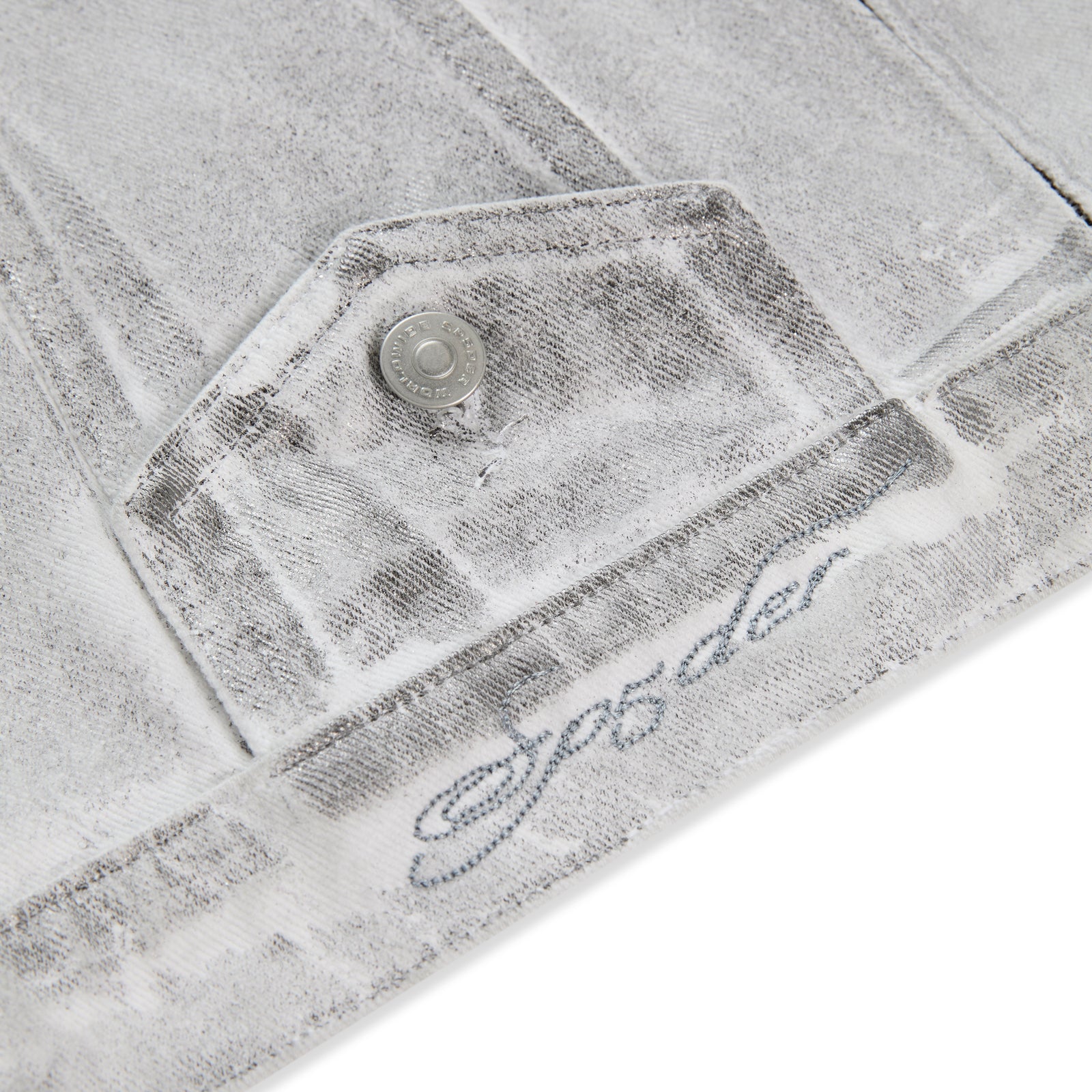 Platinum Trucker Jacket: Close-up of spray-effect denim with flap pocket, snap button, and "SP5DER" embroidery.