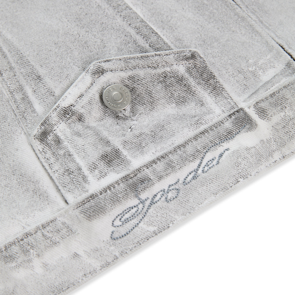 Platinum Trucker Jacket: Close-up of spray-effect denim with flap pocket, snap button, and "SP5DER" embroidery.