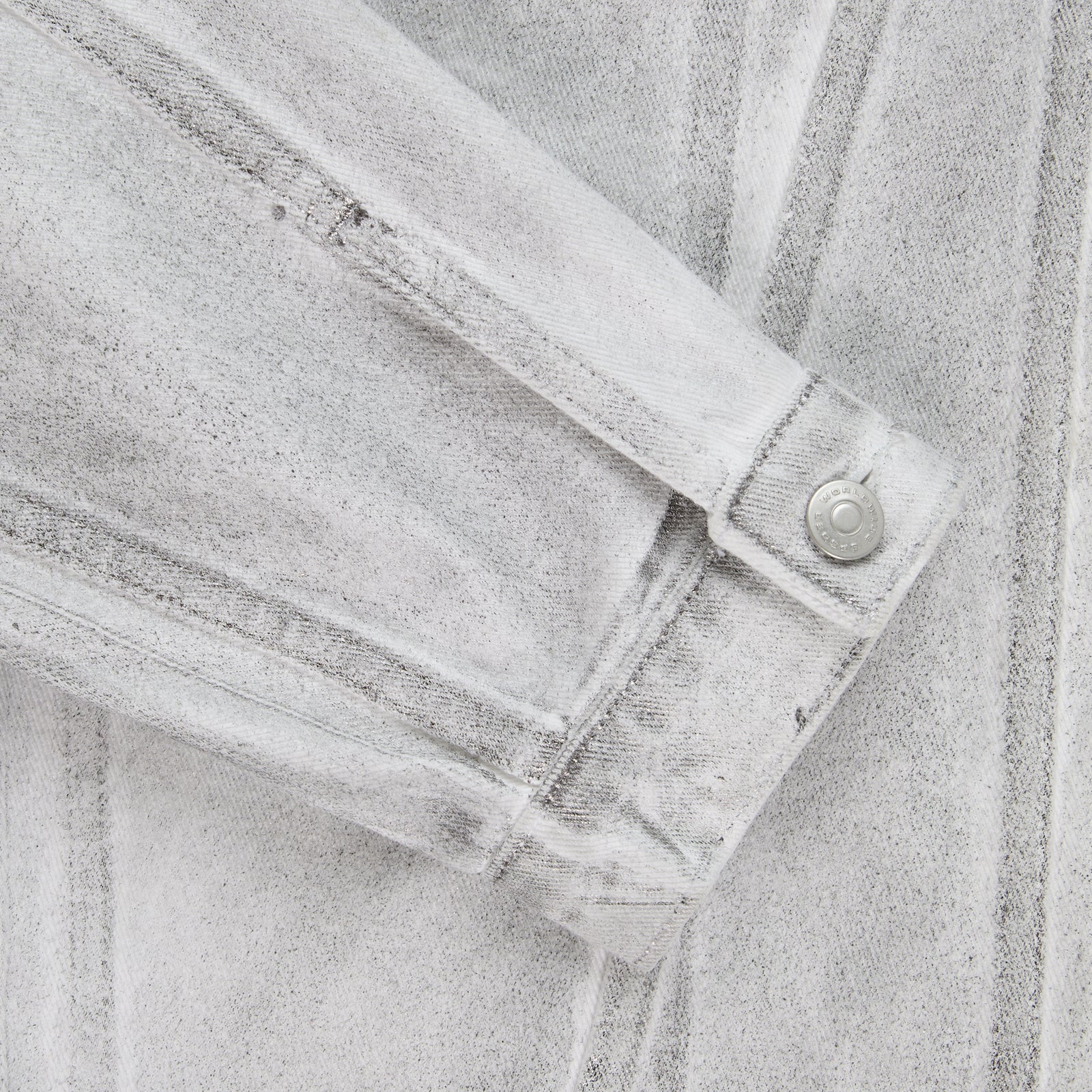 Close-up of a platinum spray-effect denim trucker jacket sleeve with a snap button cuff.