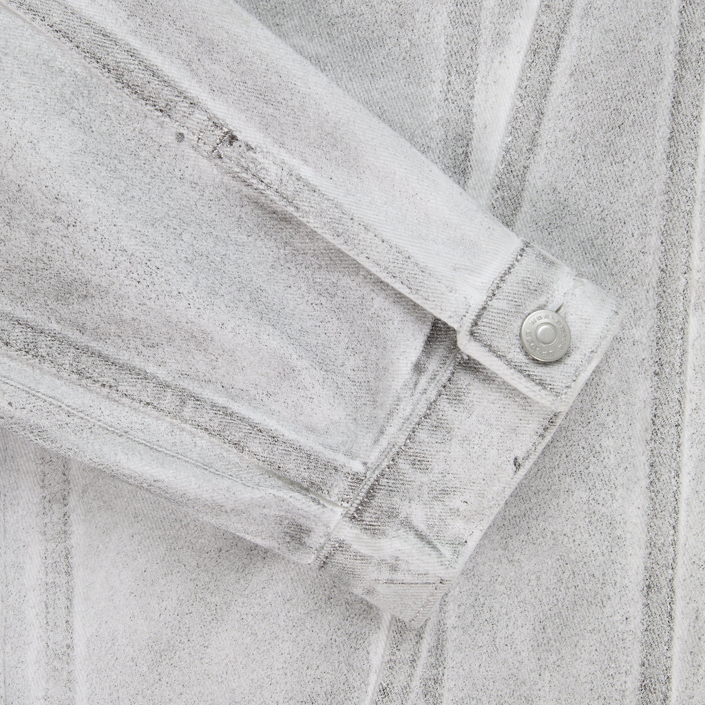Close-up of a platinum spray-effect denim trucker jacket sleeve with a snap button cuff.