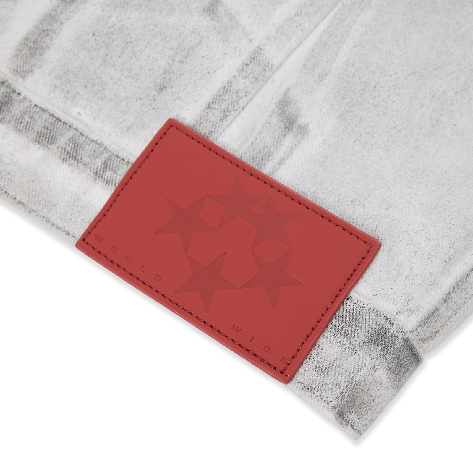 Close-up of a red leather patch with embossed stars and "WORLD WIDE" on a platinum spray-effect denim jacket.