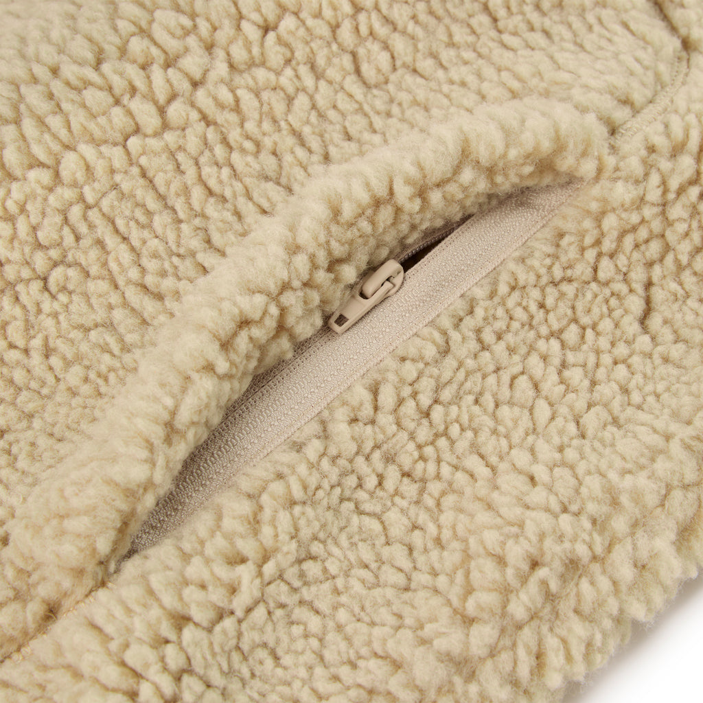 Close-up of a beige sherpa fleece jacket with a zipped welt pocket.