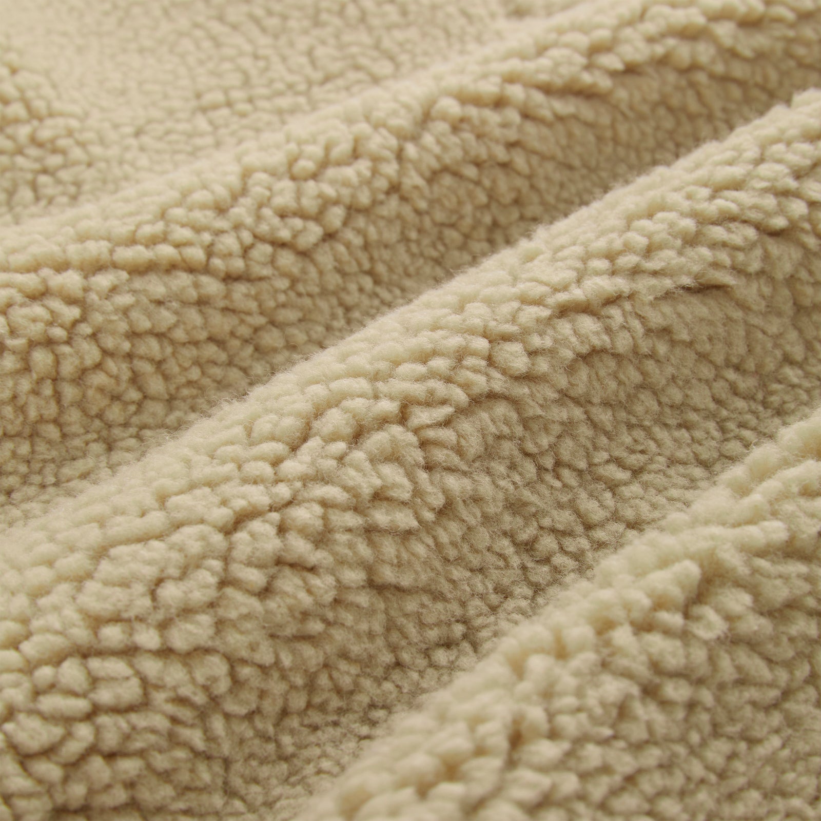 Close-up of a beige sherpa teddy fleece fabric, showing its soft, textured loops and folds.