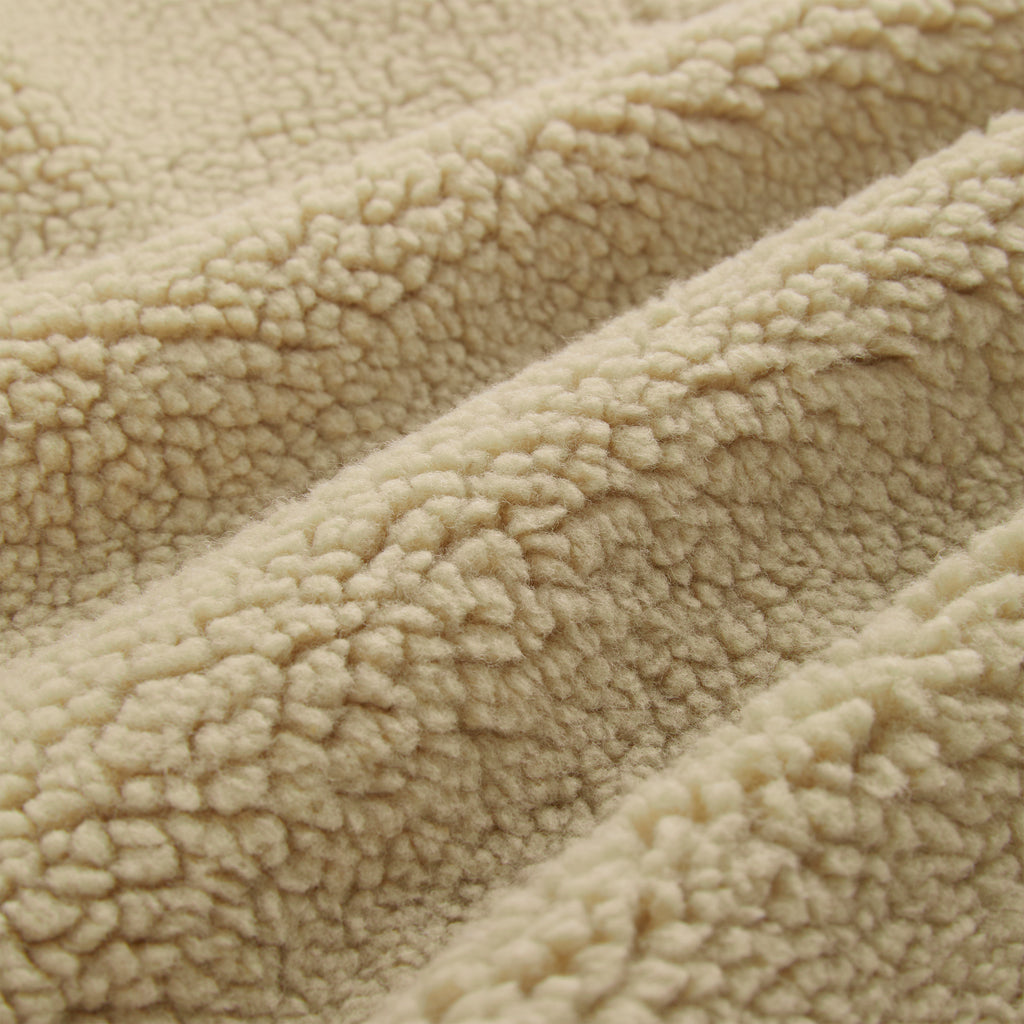 Close-up of a beige sherpa teddy fleece fabric, showing its soft, textured loops and folds.