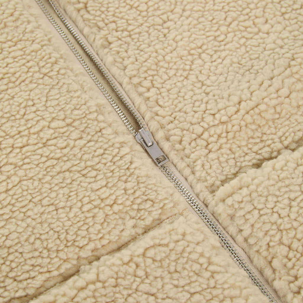Close-up of a beige teddy sherpa fleece zip-up jacket with a silver zipper.