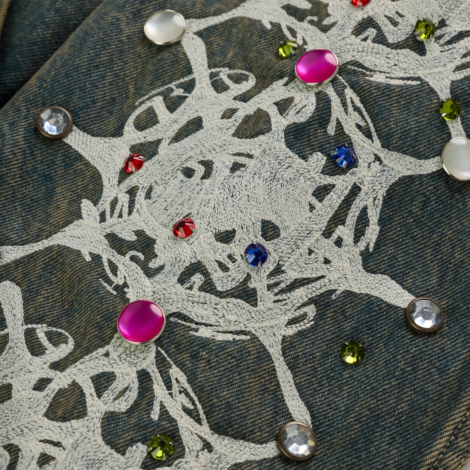 Faded denim jacket sleeve with white web print and colorful rhinestone embellishments.