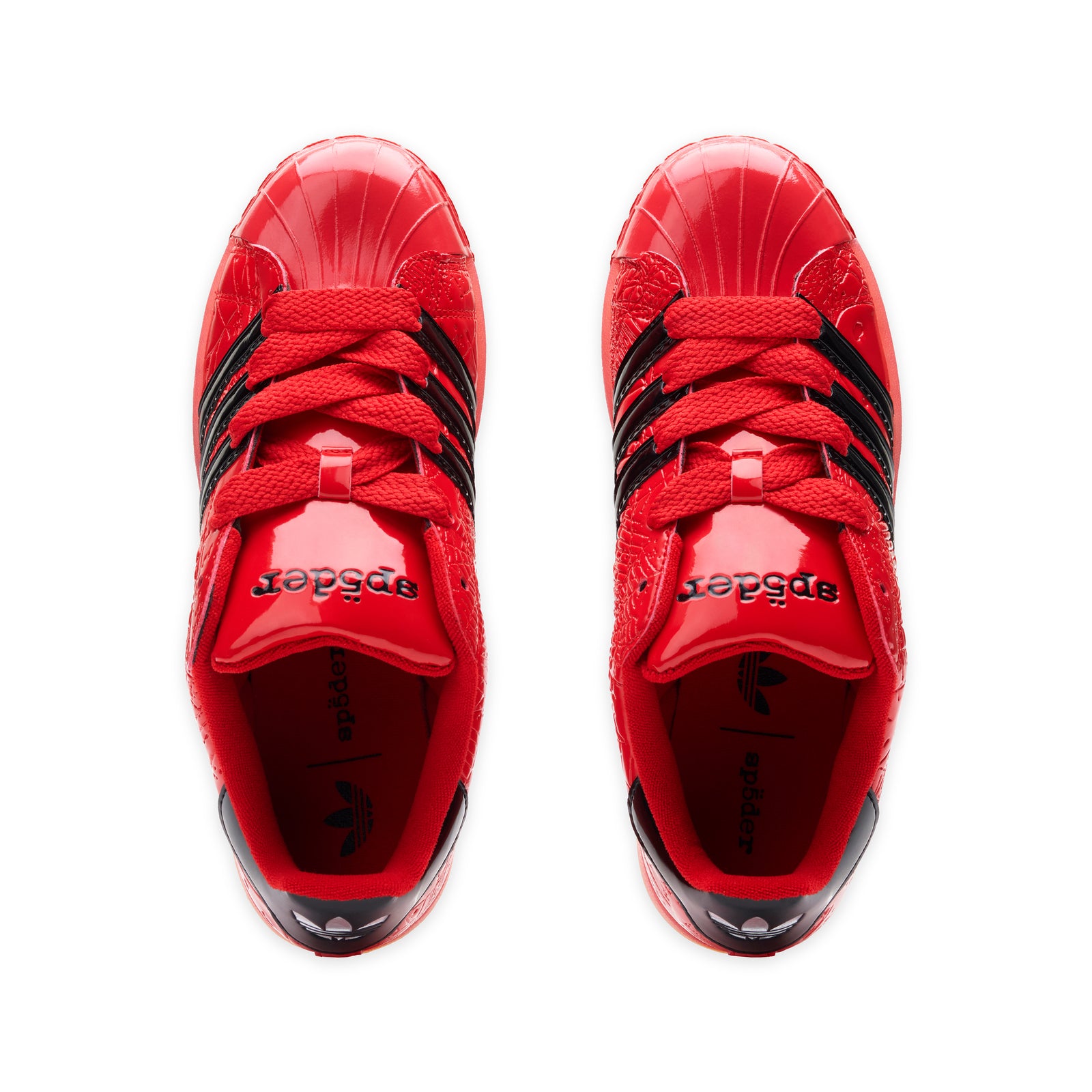Red SP5DER x ADIDAS SUPERSTAR sneakers with glossy patent leather, black stripes, and "sp5der" branding.