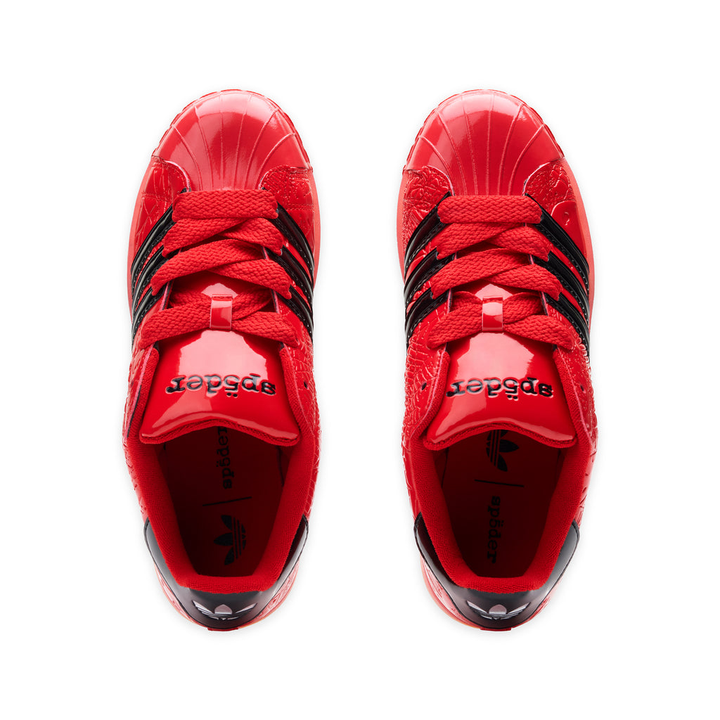 Red SP5DER x ADIDAS SUPERSTAR sneakers with glossy patent leather, black stripes, and "sp5der" branding.
