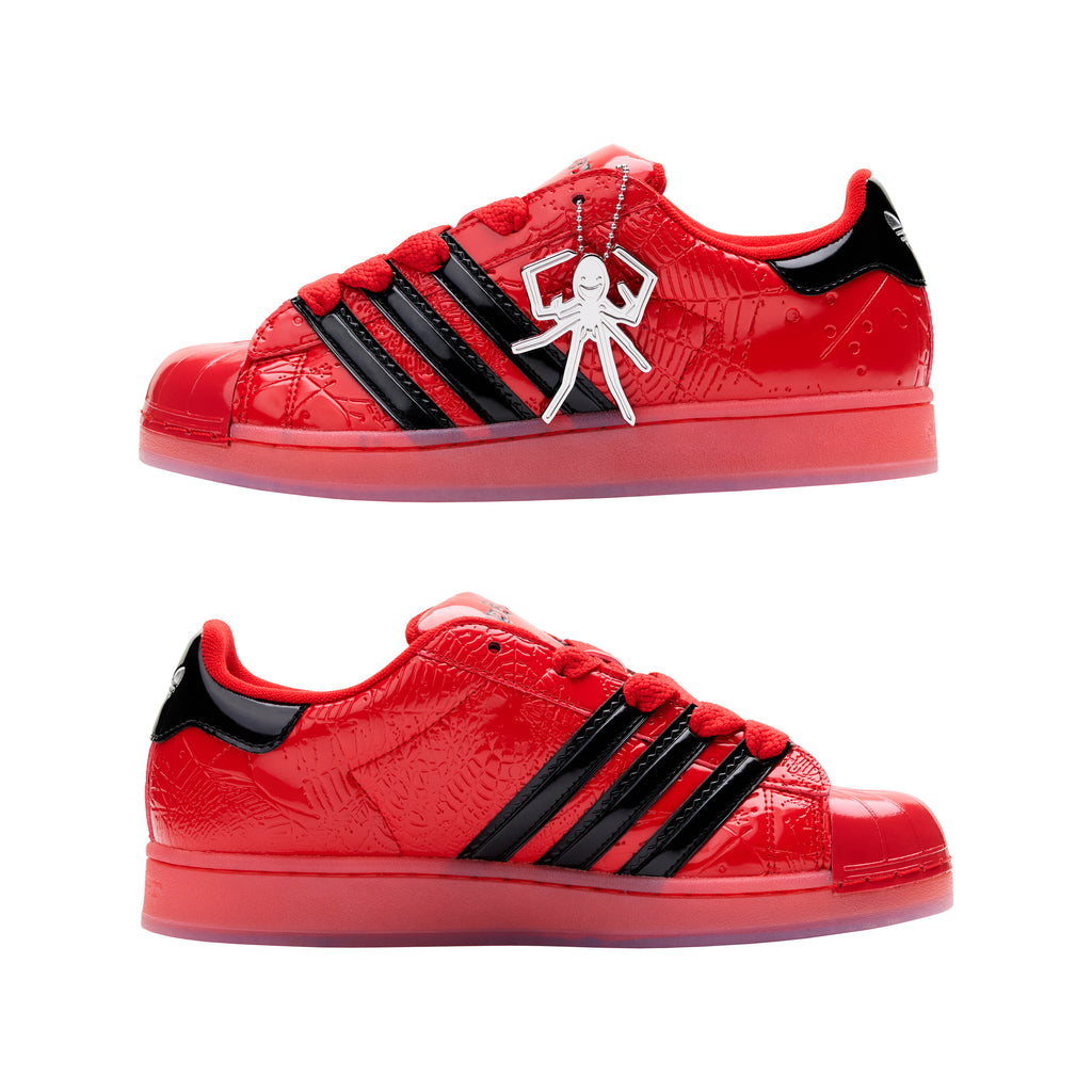 Red glossy patent leather Adidas Superstar sneakers with black stripes and a silver spider charm.