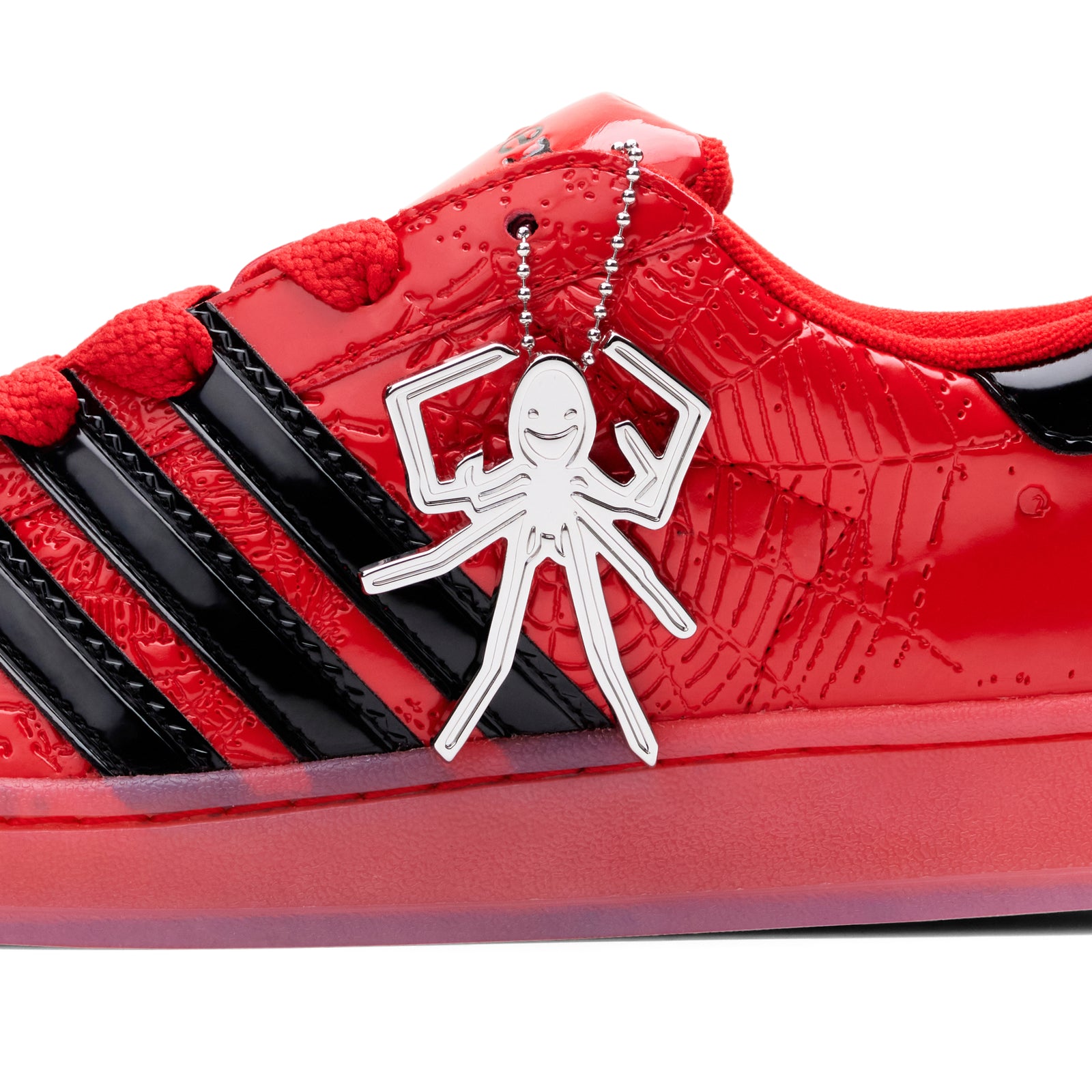 Red SP5DER x ADIDAS SUPERSTAR with glossy patent leather, black stripes, and a silver spider charm.