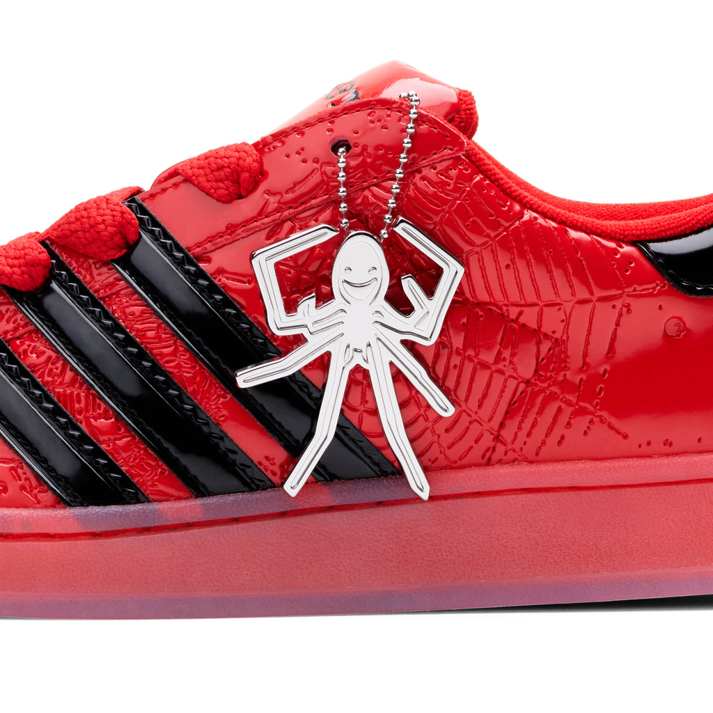 Red SP5DER x ADIDAS SUPERSTAR with glossy patent leather, black stripes, and a silver spider charm.