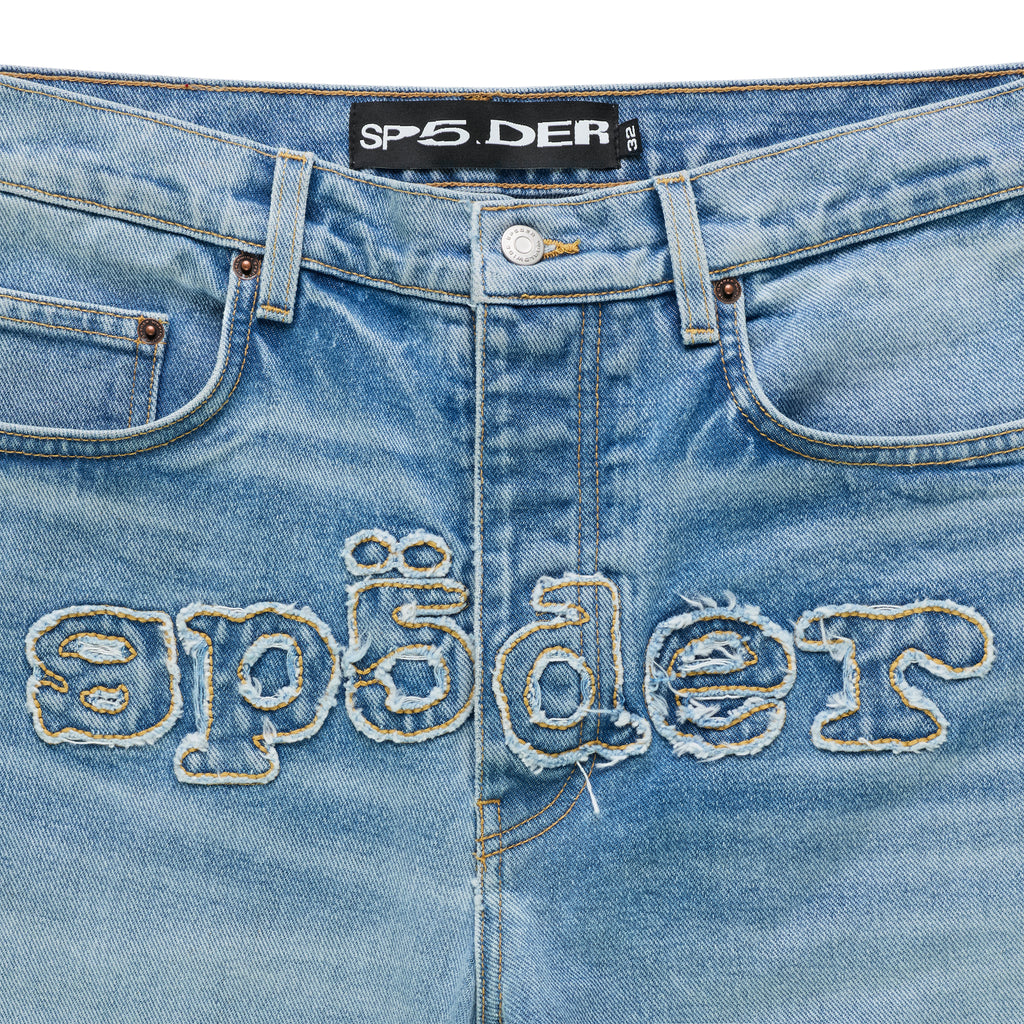 Light wash distressed denim jeans with frayed "SP5DER" logo embroidery across the crotch.