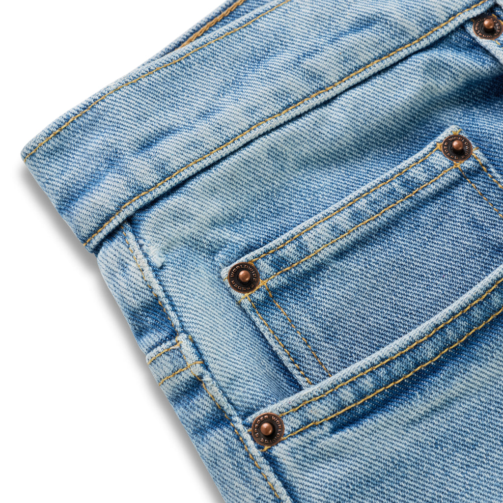 Light wash distressed denim jeans with custom branded hardware and yellow stitching.
