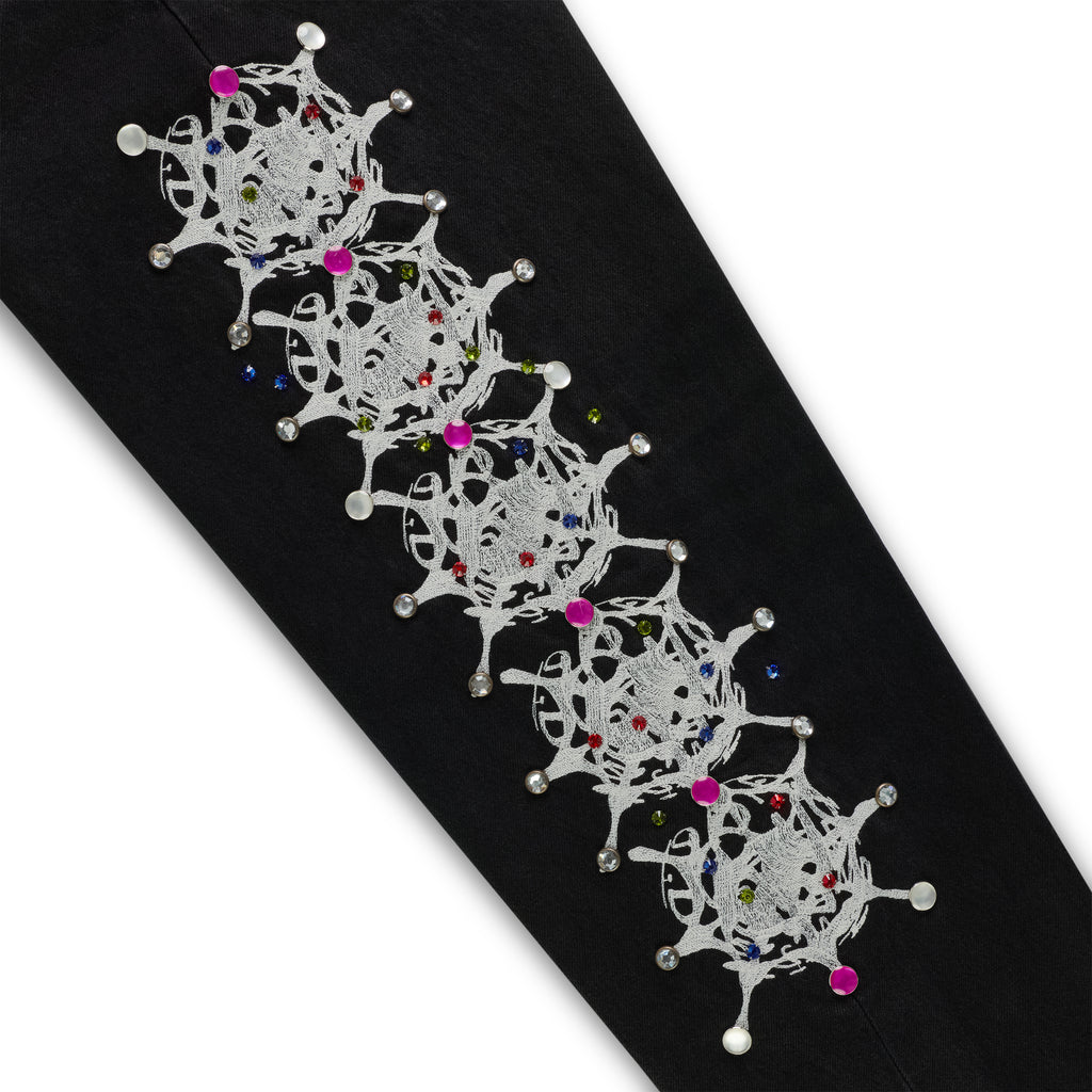 Black denim pant leg with white web print and colorful rhinestone embellishments.