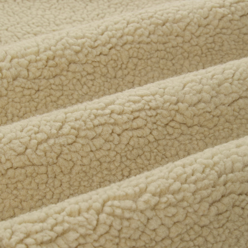 Close-up of soft, cream-colored sherpa fleece fabric with visible texture and folds.