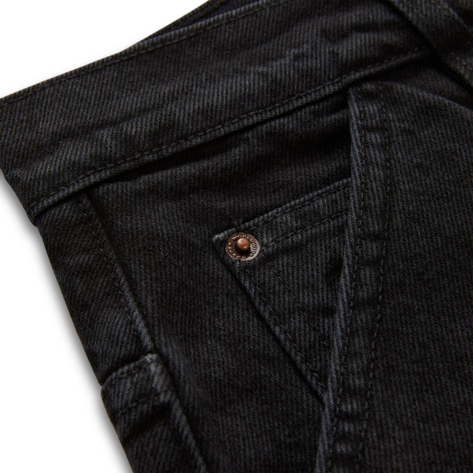 Close-up of faded black denim pants with custom branded hardware and distressed detailing.