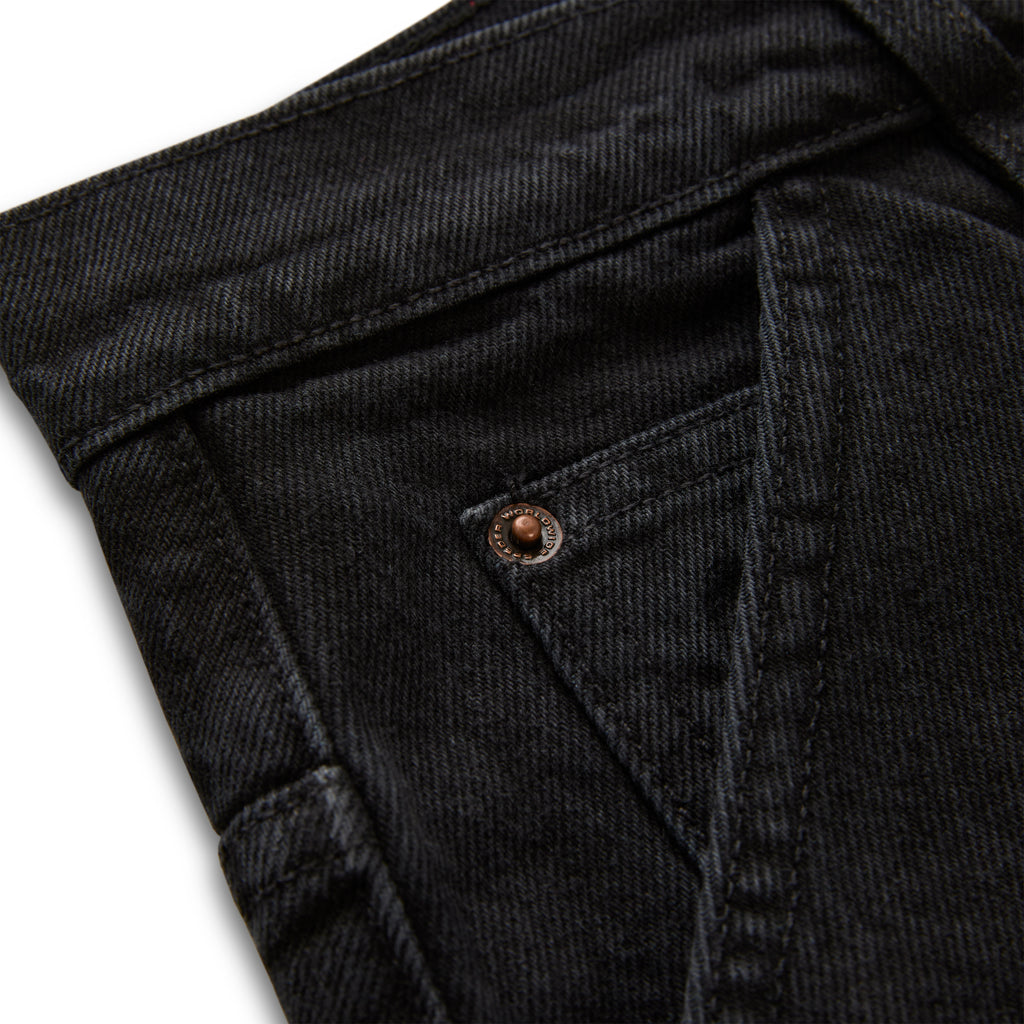 Close-up of faded black denim pants with custom branded hardware and distressed detailing.
