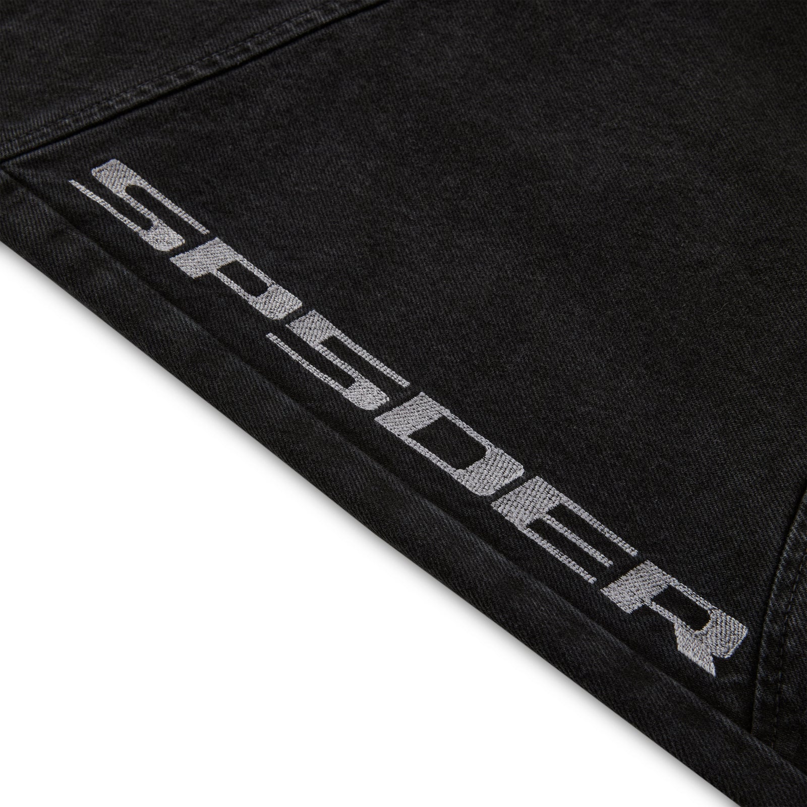 Close-up of black faded wash denim pant with "SP5DER" logo printed on the leg.
