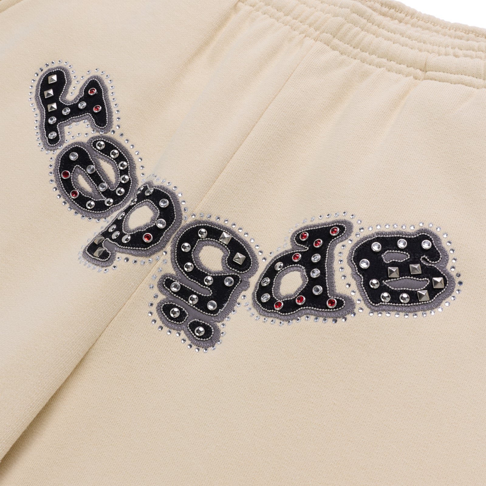 Beige cotton fleece sweatpants with "OG LOGO" appliqué embellished with mixed metal studs and red stones.