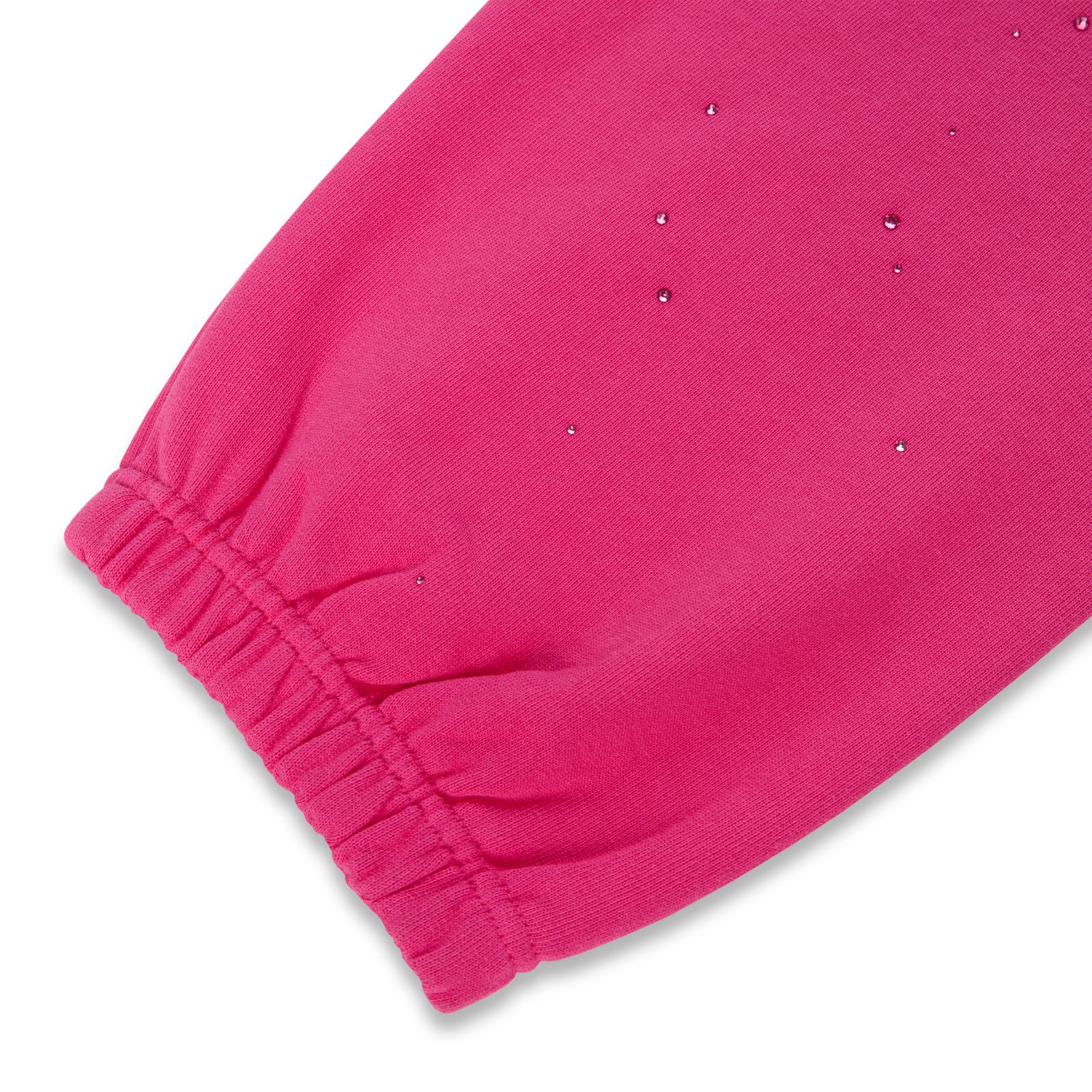 Close-up of a vibrant pink cotton fleece sweatpant leg with scattered rhinestone embellishments and an elasticized cuff.