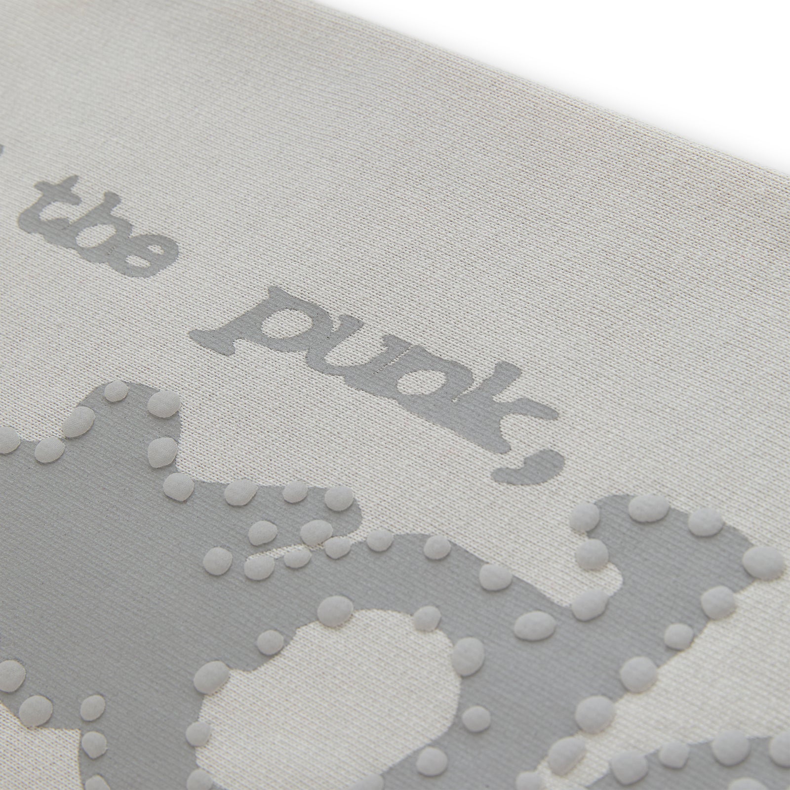 Close-up of light grey cotton fleece sweatpant with puff print "P*NK SP5DER" text and stars.