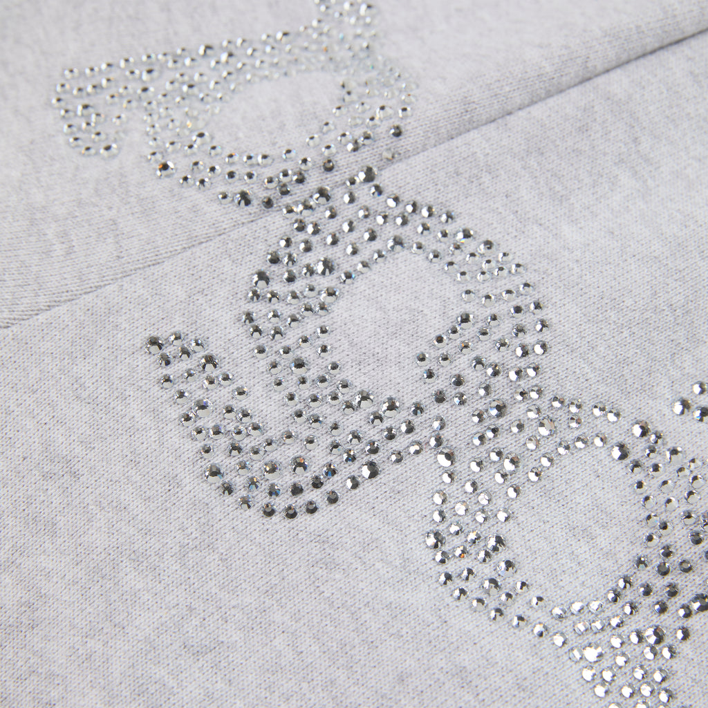 Close-up of gray cotton fleece sweatpants with "SP5DER" text and "5" star design in rhinestones.