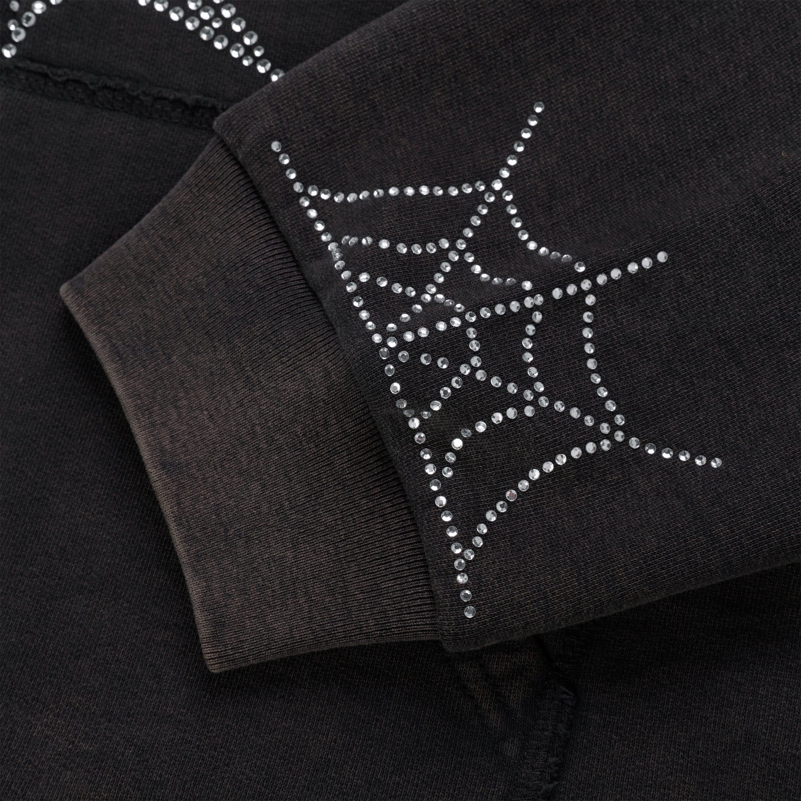Close-up of a black cotton fleece hoodie sleeve with a rhinestone spider web design on the ribbed cuff.