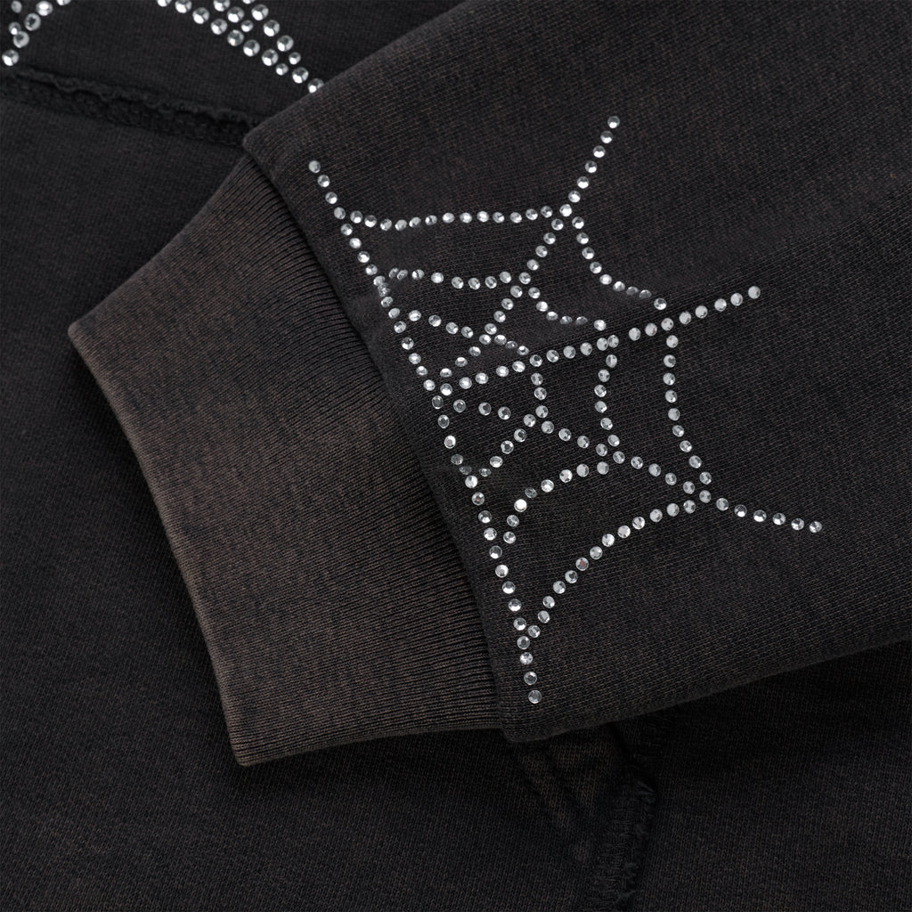 Close-up of a black cotton fleece hoodie sleeve with a rhinestone spider web design on the ribbed cuff.