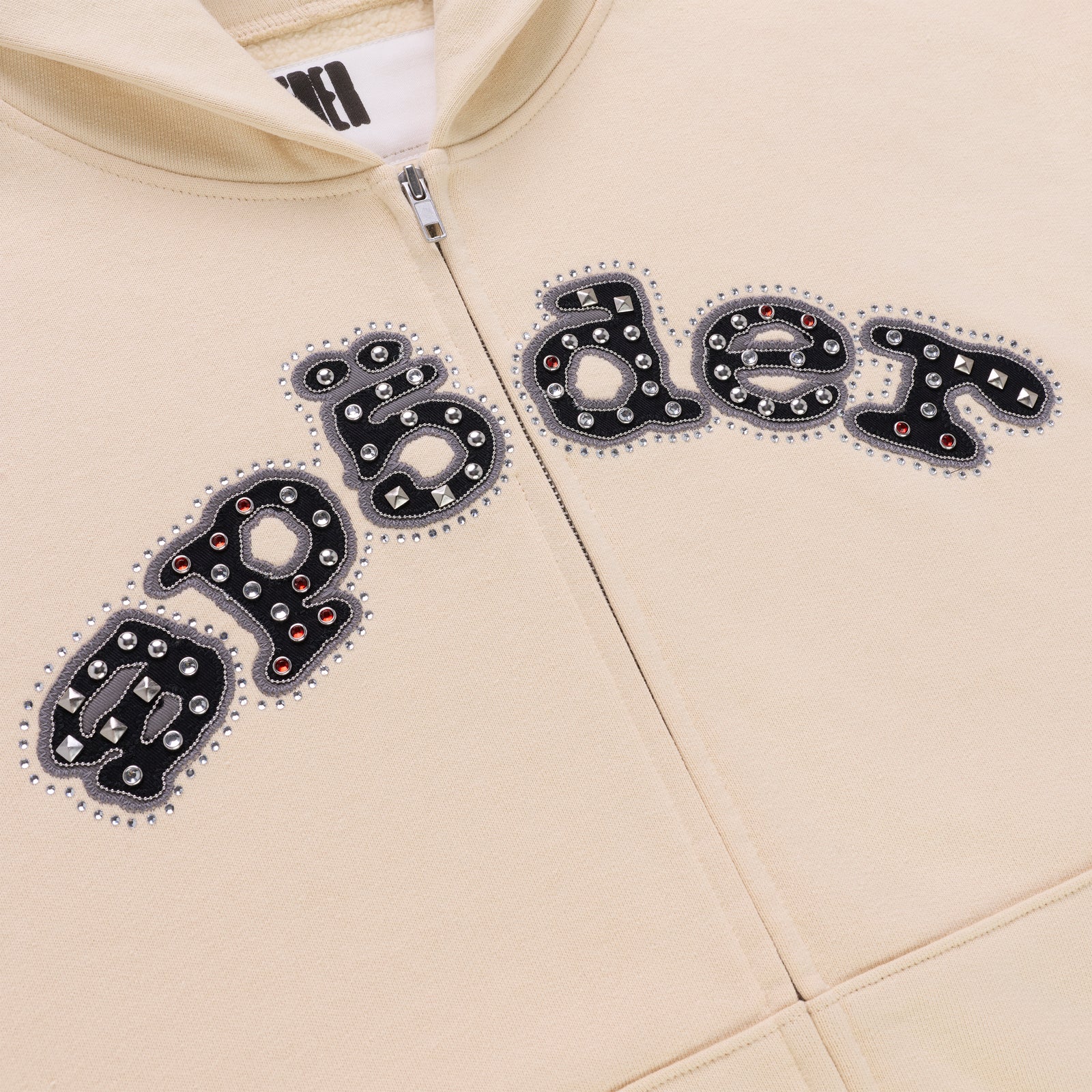 Cream cotton fleece zip hoodie with "Mixed Stone OG" logo embellished with metal studs, rivets, and spikes.
