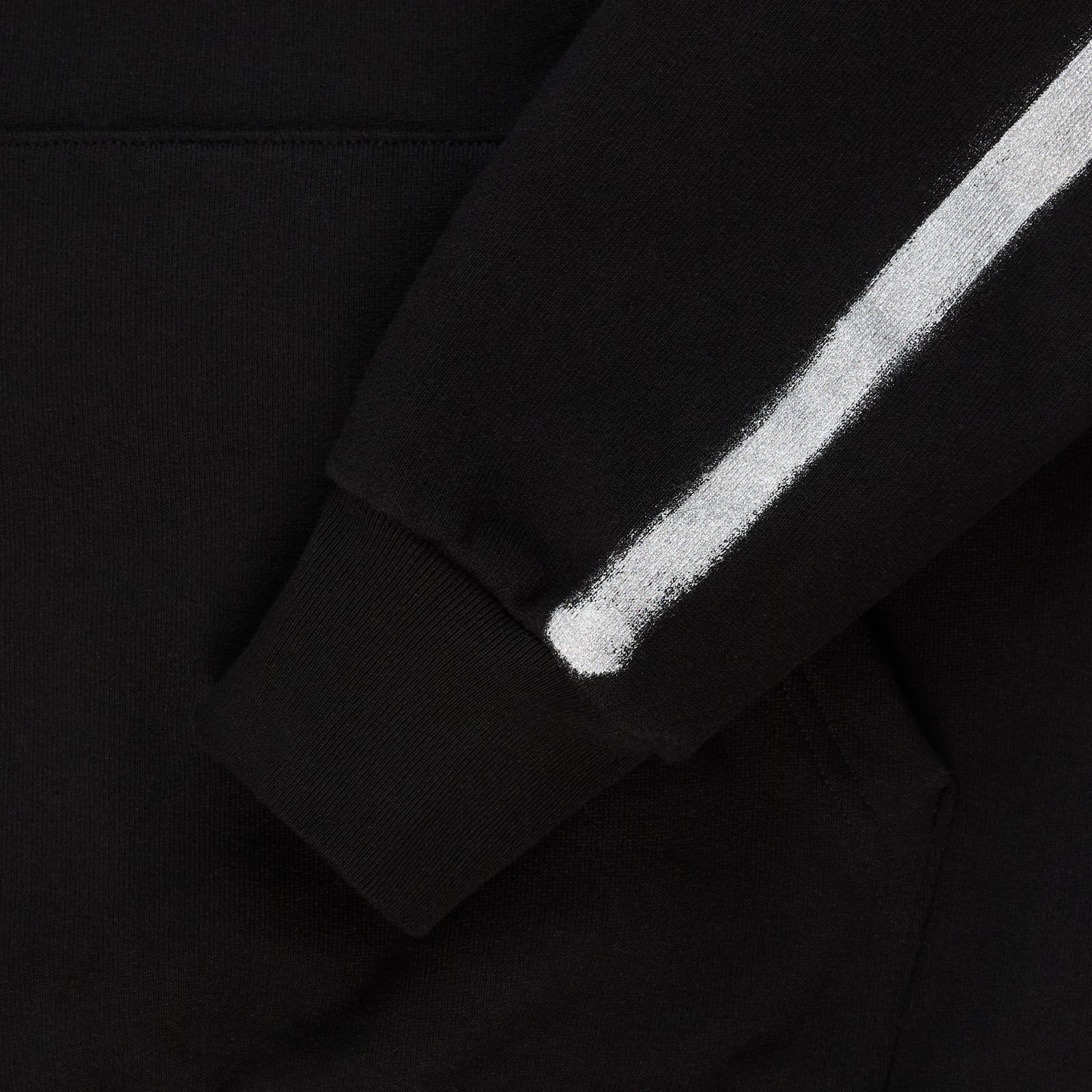 Black cotton fleece hoodie sleeve with white sprayed-effect stripe and ribbed cuff.