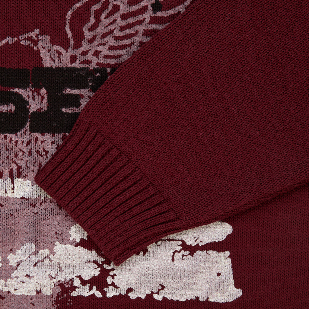 Maroon knit sweater with graphic print, ribbed cuffs, and textured fabric.